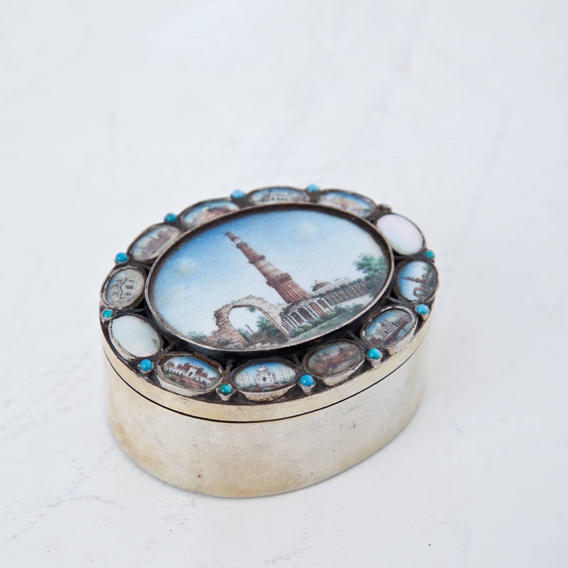 Oval silver box with miniature depictions of important monuments of India. In the center is a large depiction of Qutb Minar, the famous watchtower of Delhi. In the smaller medallions, one can find among others a depiction of the Taj Mahal.