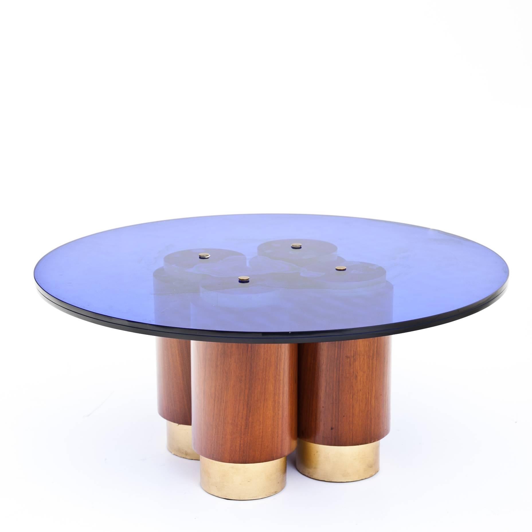Round coffee table on four separate cylindrical legs with brass colored bases. The cobalt blue tabletop shows signs of age and use.