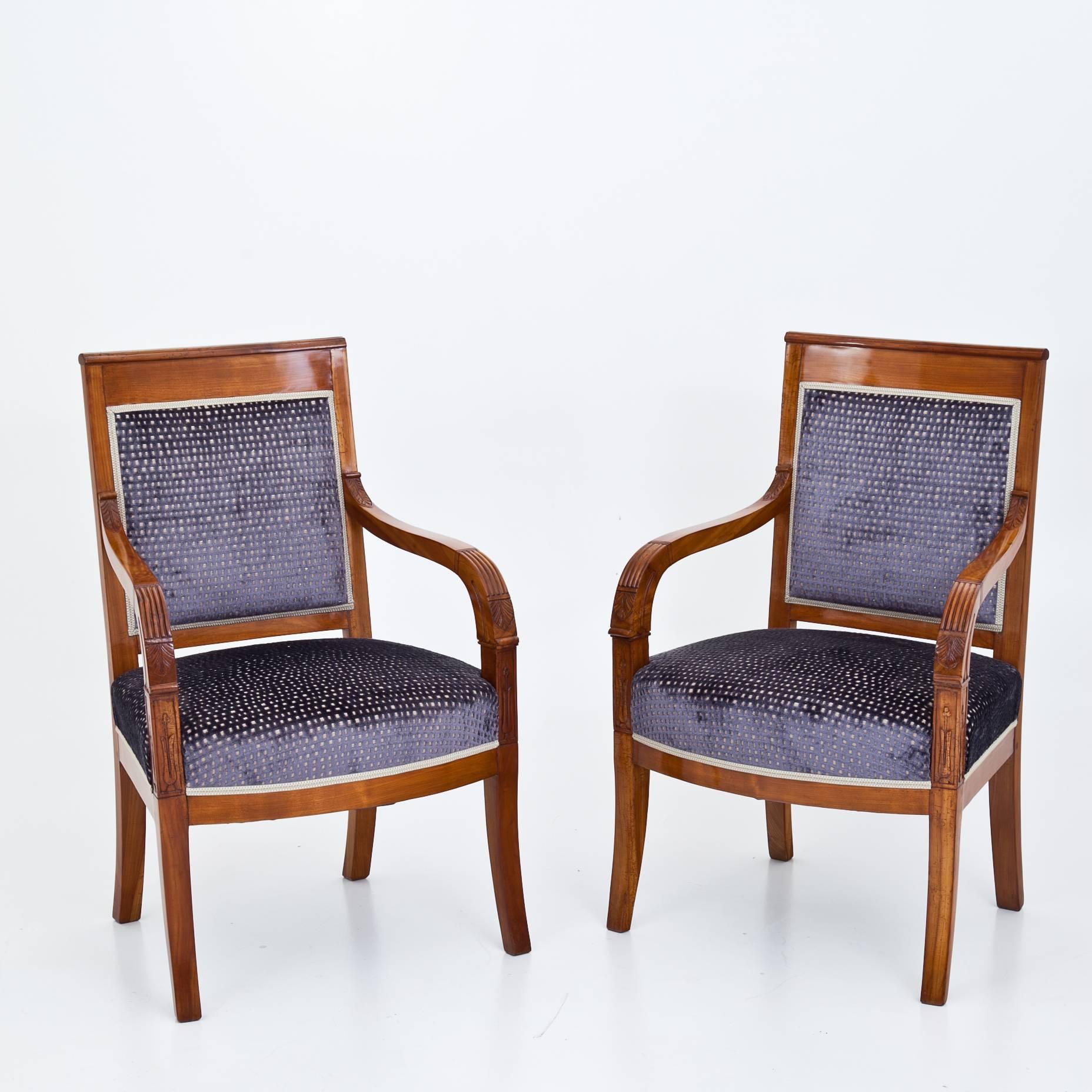 Pair of French cherrywood armchairs of the first half of the 19th century. The backrests and seats are reupholstered with a high quality purple and gold fabric, and the armrests show exquisite carvings. The chairs are very elegant and in a very good
