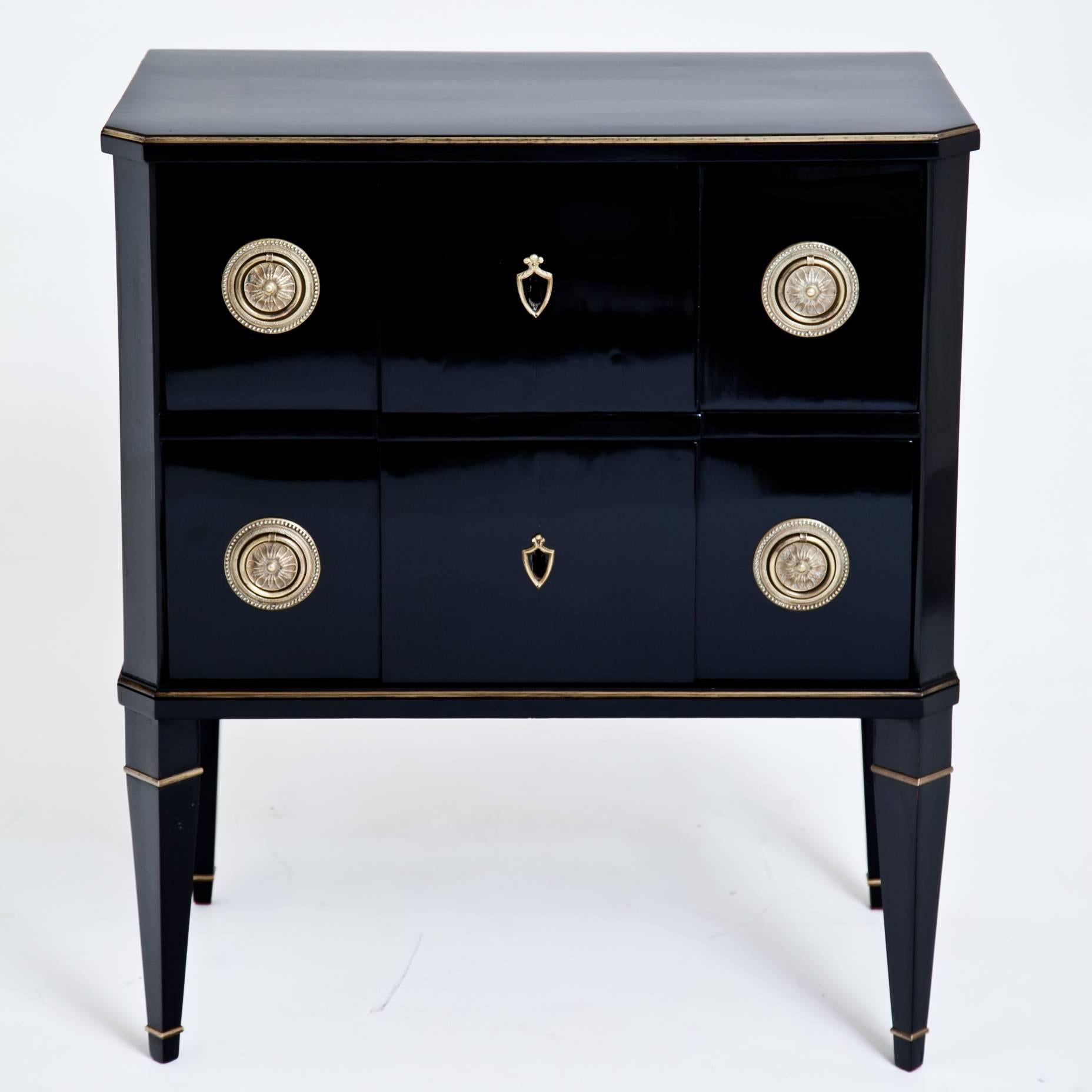 Small black neoclassical chest of drawers on tapered feet with brass details. The ebonized body shows slanted edges and has two drawers with brass fittings. The chest was ebonized later and is in a restored condition.
 