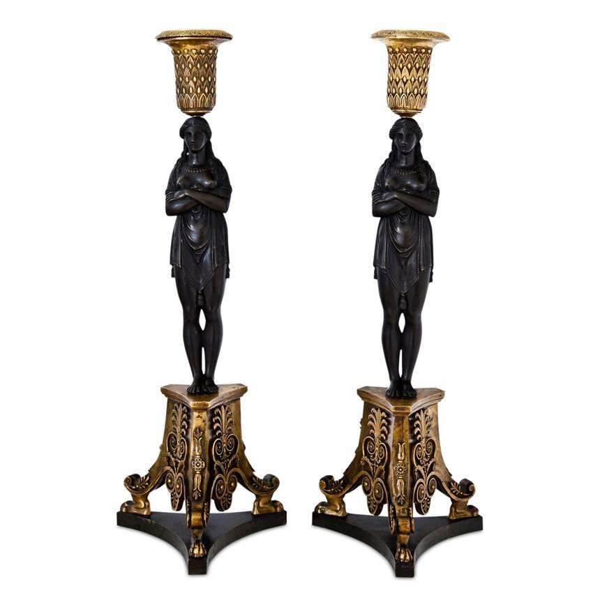 Empire candlesticks on a trefoil base with bronze bases and nozzles with palmetto decor as well as caryatids with crossed arms. For the model, compare Thomire-Duterme et Cie from 1809 for the second resp. large Salon in the small appartement of the