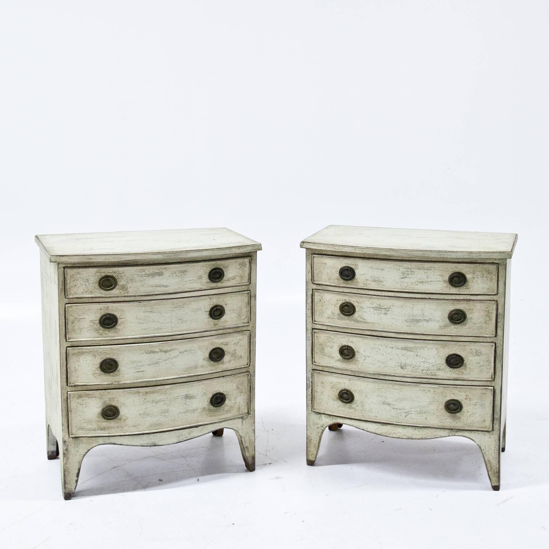 Pair of English chests of drawers on low legs with a softly curved skirt. The corpus has four drawers and a slightly curved front. The crème-white paint is slightly worn.