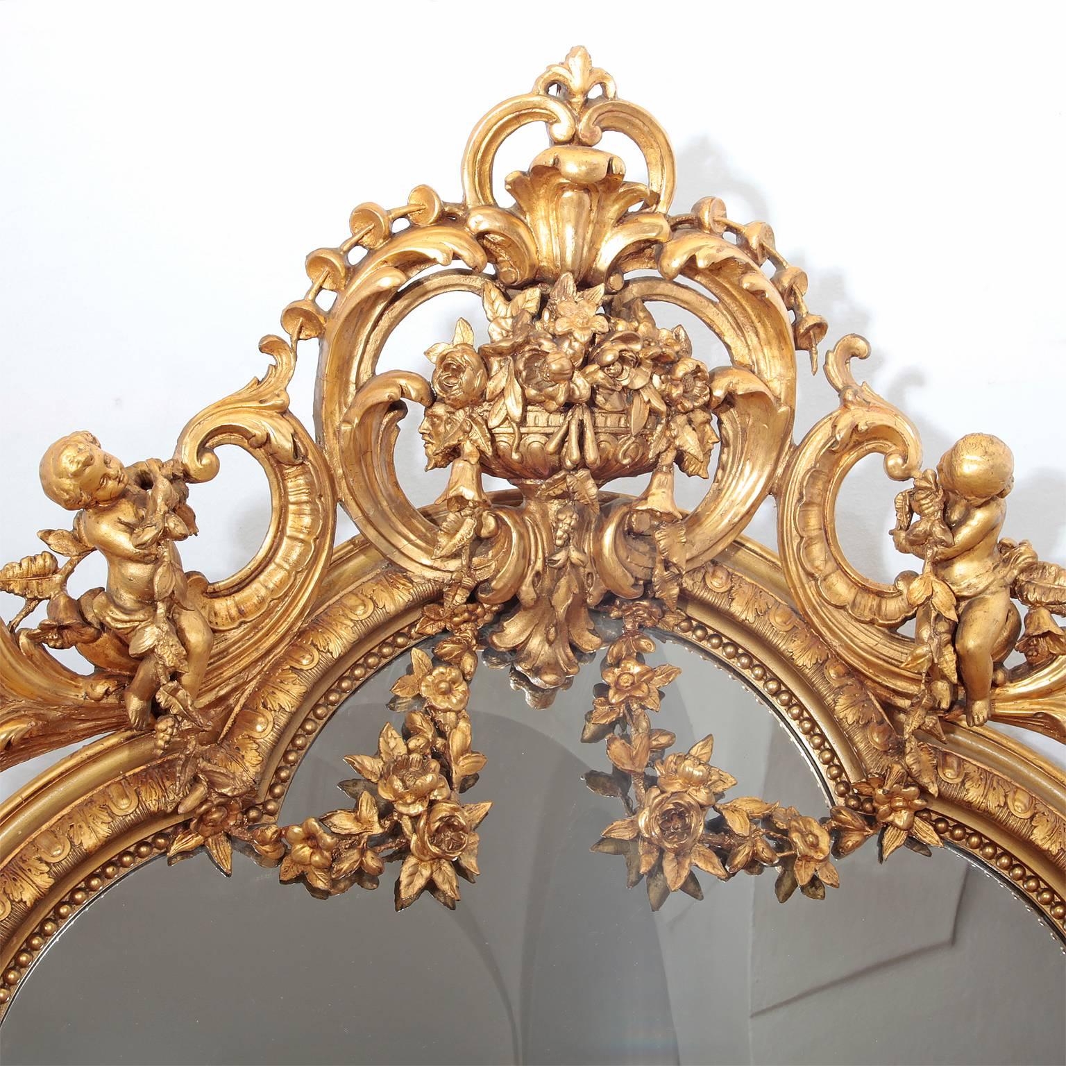 Large Mirror of the Napoleon III period. The gilded frame is decorated with classical friezes and has a very elaborately designed headpiece with c-shaped rocailles, festoons and cherubs surrounding an amphora.