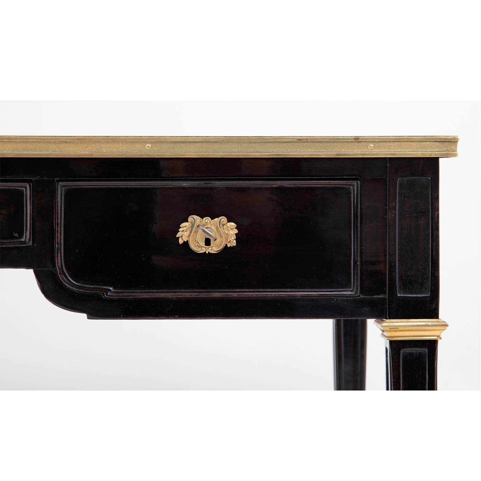 Ebonised writing desk in Louis-Seize-Style with three drawers and a leather writing surface. The table stands on tapered square feet and is decorated with bronze ornaments in the shape of strips, rocailles and leaves.