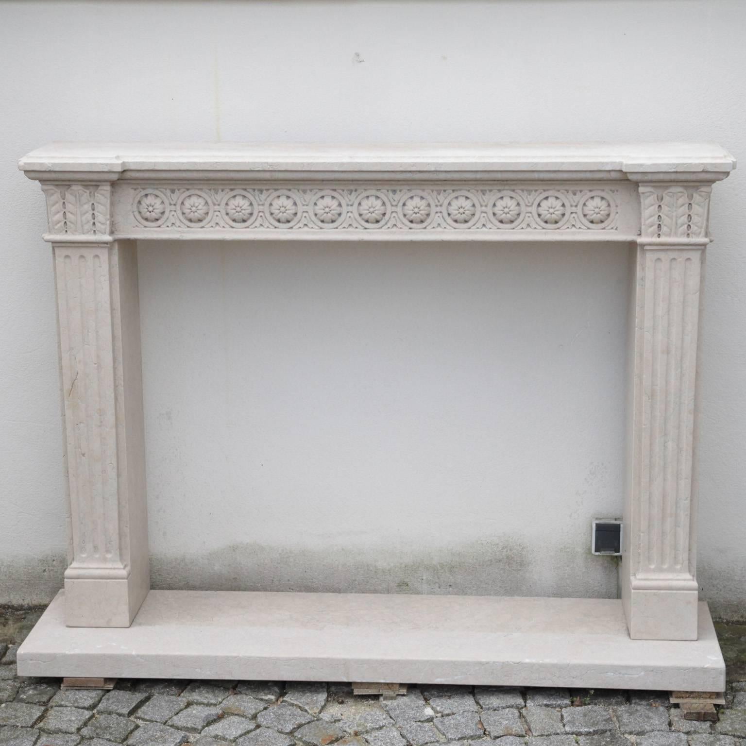 Marble fireplace frame with flower frieze in the top ledge and leaf reliefs on the corners. Two fluted pillars make up either side of the frame and the whole thing stands on a marble plate. The surface is very fine. This piece is a unique