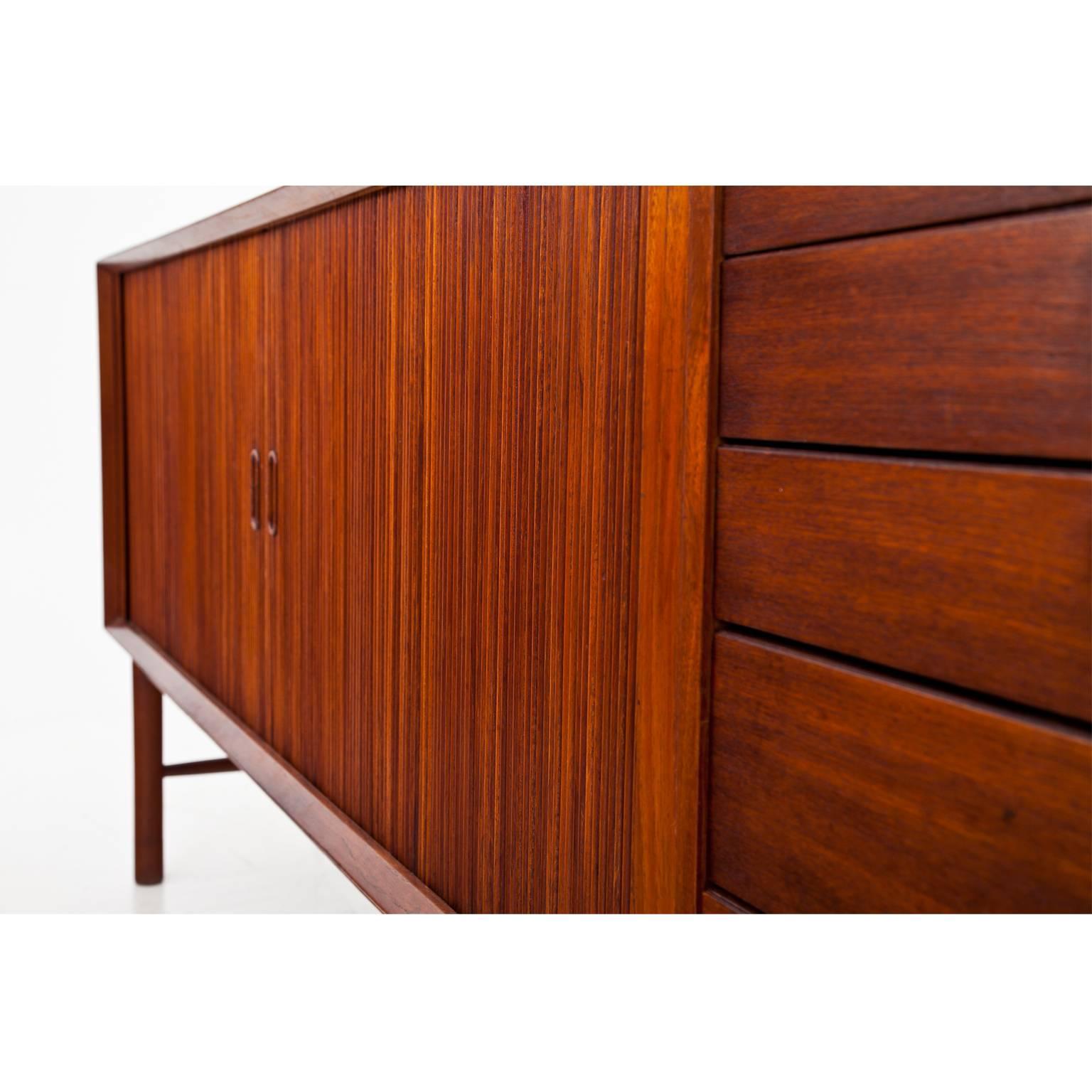 Long sideboard standing on round feet. The rectangular body has two sliding doors and five-drawers in the style of the sideboards by Orla Mølgaard-Nielsen und Peter Hvidt from the 1950s. The sideboard is in a restored condition.