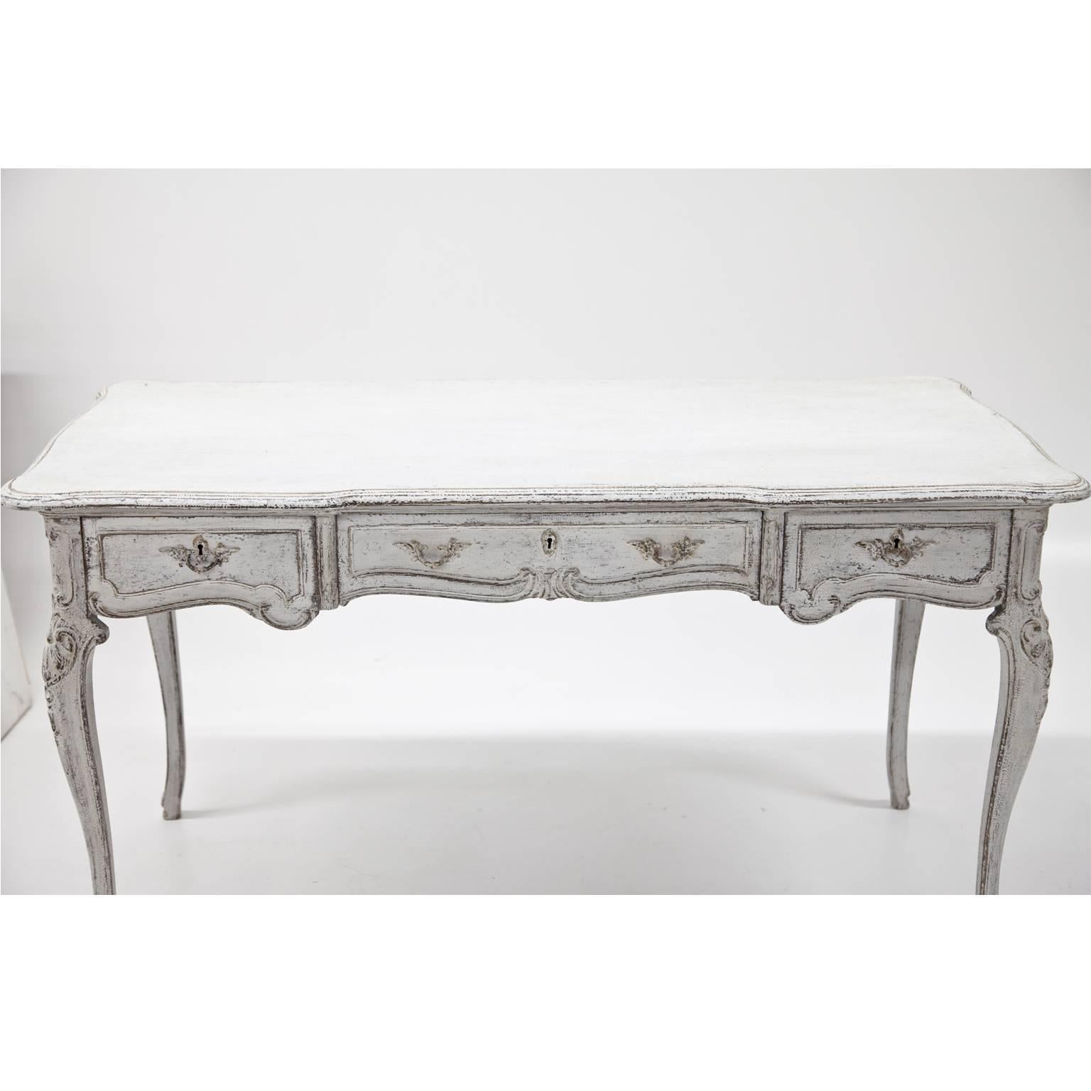 White Gustavian-style table with capriole legs and three drawers. The tabletop has a wavy edge, the drawers are decorated with rocaille and acanthus leaves carvings. The paint is redone and has a slightly worn look to it, giving it a beautiful