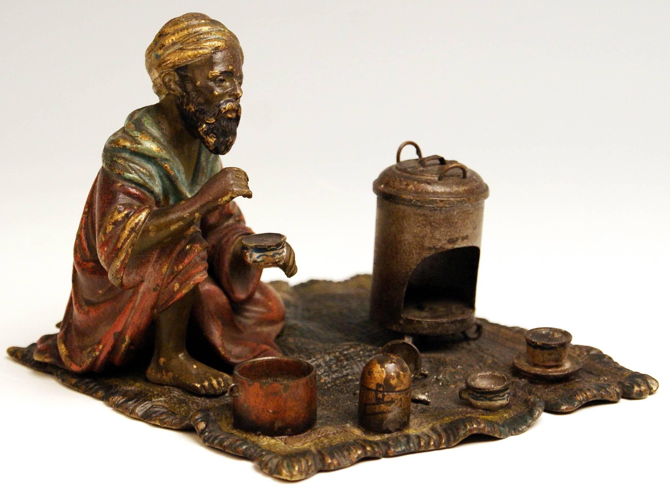 Stunning bronze figurine: Arab man situated on carpet 

An Arab man is busy with preparation of tea: He sits on carpet and holds a cup of tea in left hand. There is an oven visible next to him / some cups, a spoon, a lidded pot and a vessel have