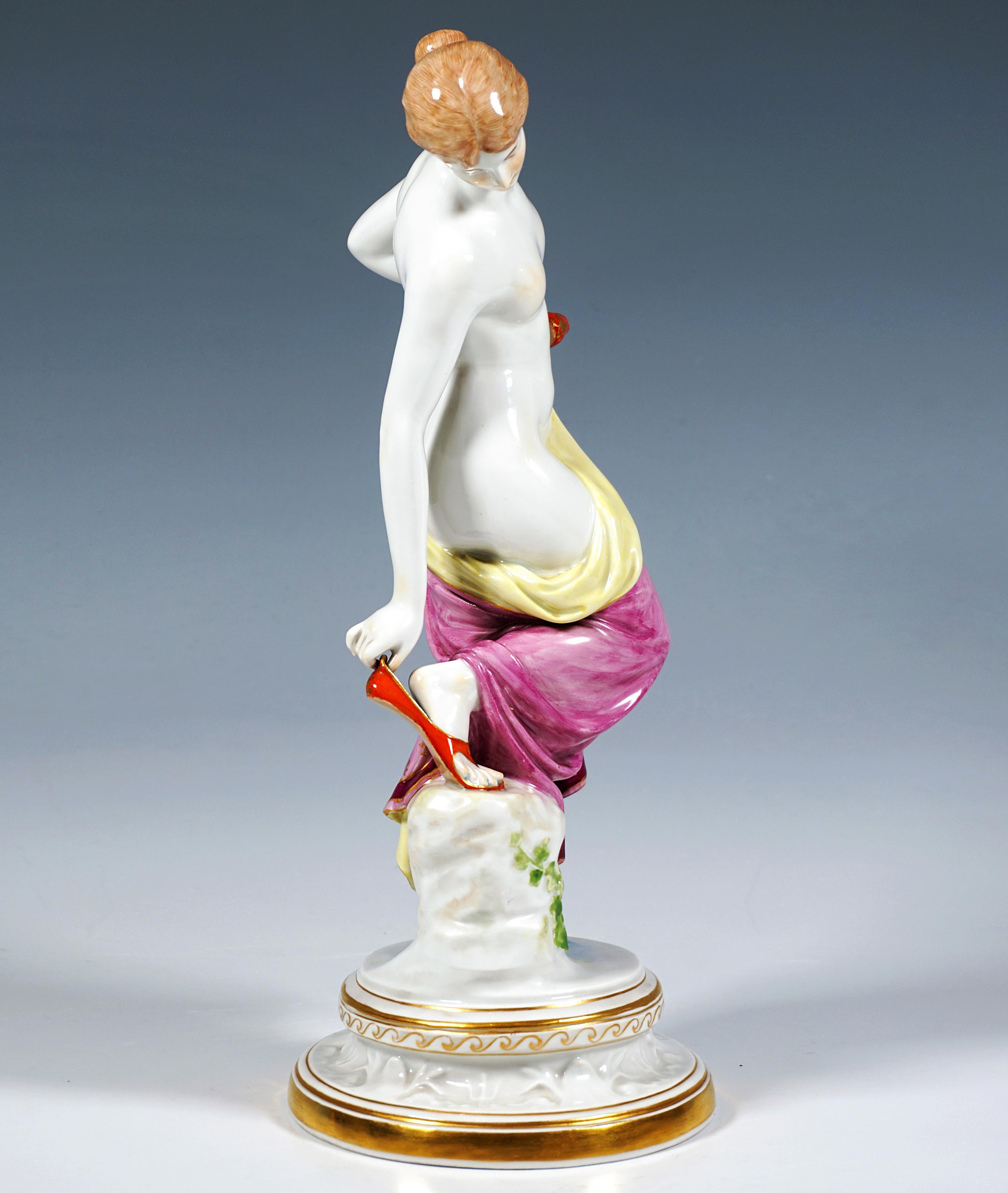 Représentation extrêmement décorative, entièrement sculptée, d'une jeune beauté nue, les cheveux attachés, couvrant sa nudité après son bain d'un tissu doucement drapé, qu'elle tient d'une main à sa hanche gauche, avec un 
Elle se glisse dans la
