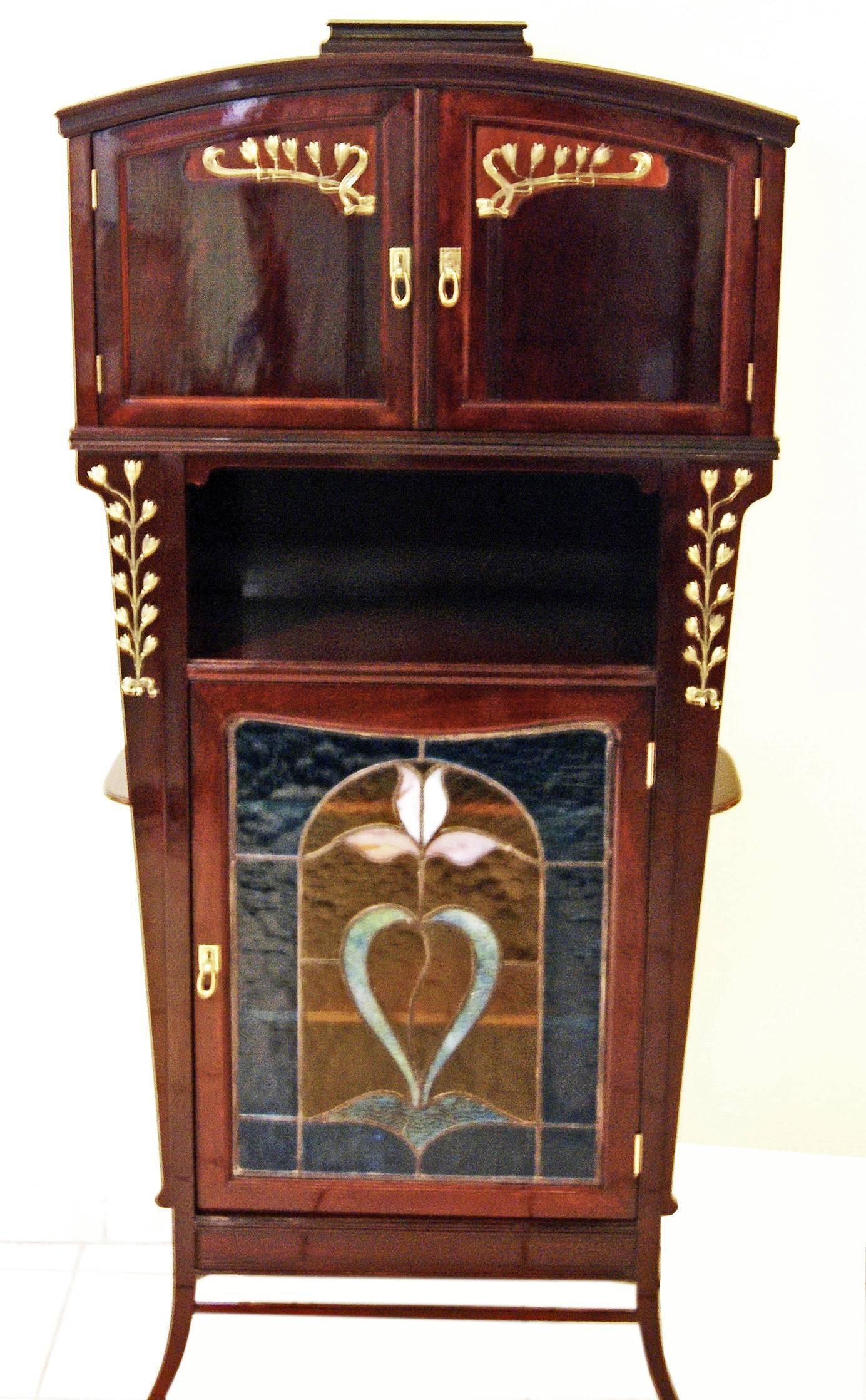 Gorgeous Art Nouveau showcase of finest manufacturing quality:

This furniture piece consists of three parts (vertical structure):
The upper part has two doors: These are stunningly decorated with finest brass mountings (blossoms of bellflowers