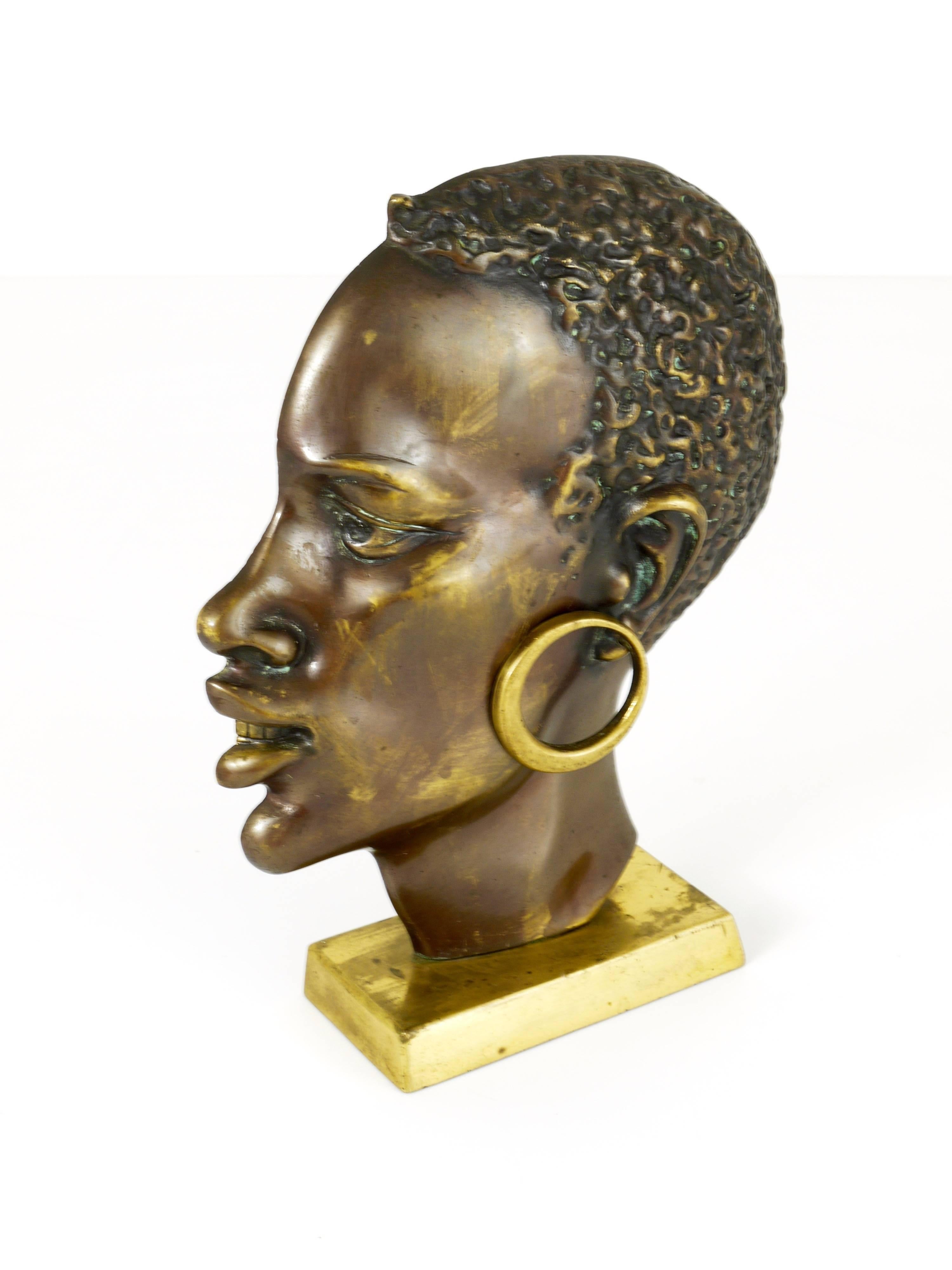 A mid-century modernist brass sculpture depicting the head of an African woman, elegantly mounted on a square base. Crafted in Austria during the 1950s, it remains in very good condition showcasing marginal patina. In the style of Werkstätte