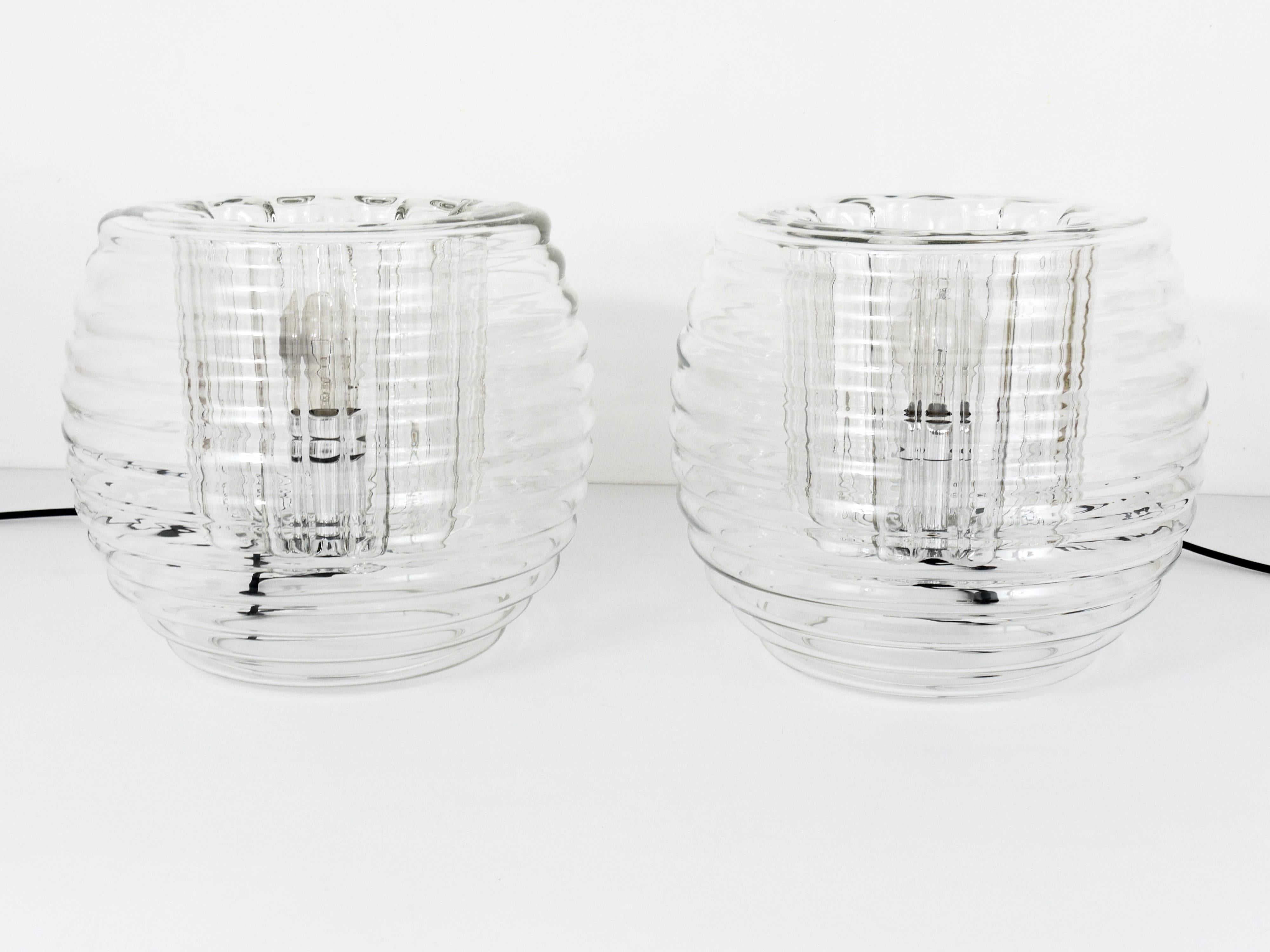 Up to two exquisite hand-blown table or side lamps dating back to the 1970s, offered separately and priced per piece. These lamps were designed by Ernest Koch & Thomas Lowy for Peill & Putzler in Germany. Crafted from a single piece of ribbed clear