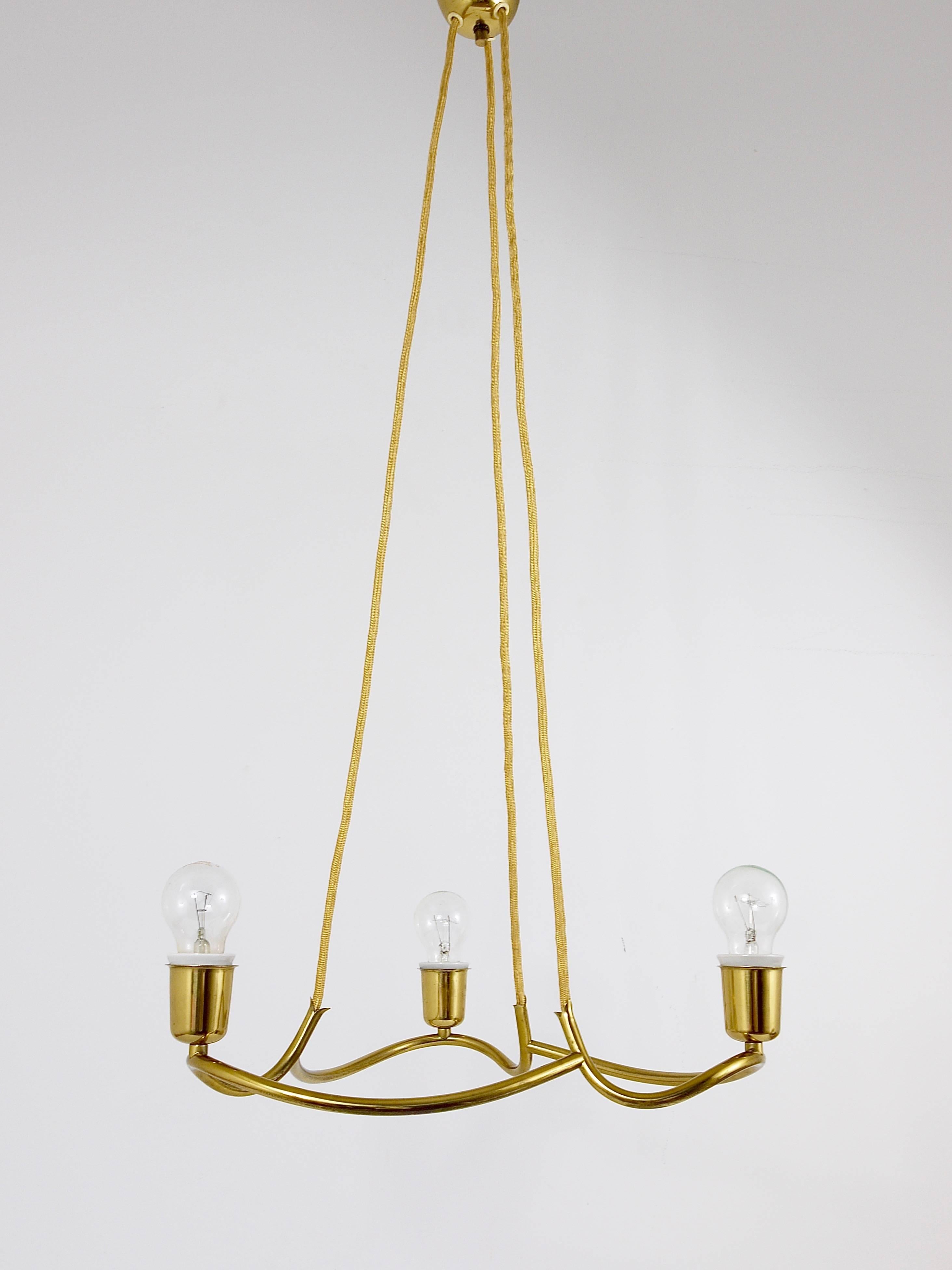 A gorgeous brass chandelier, known as the 'Heron' model, produced by J.T. Kalmar Vienna in the early 1950s. Featuring a gracefully curved brass frame, equipped with three light sources, suspended by golden fabric cords. It's in very good condition,