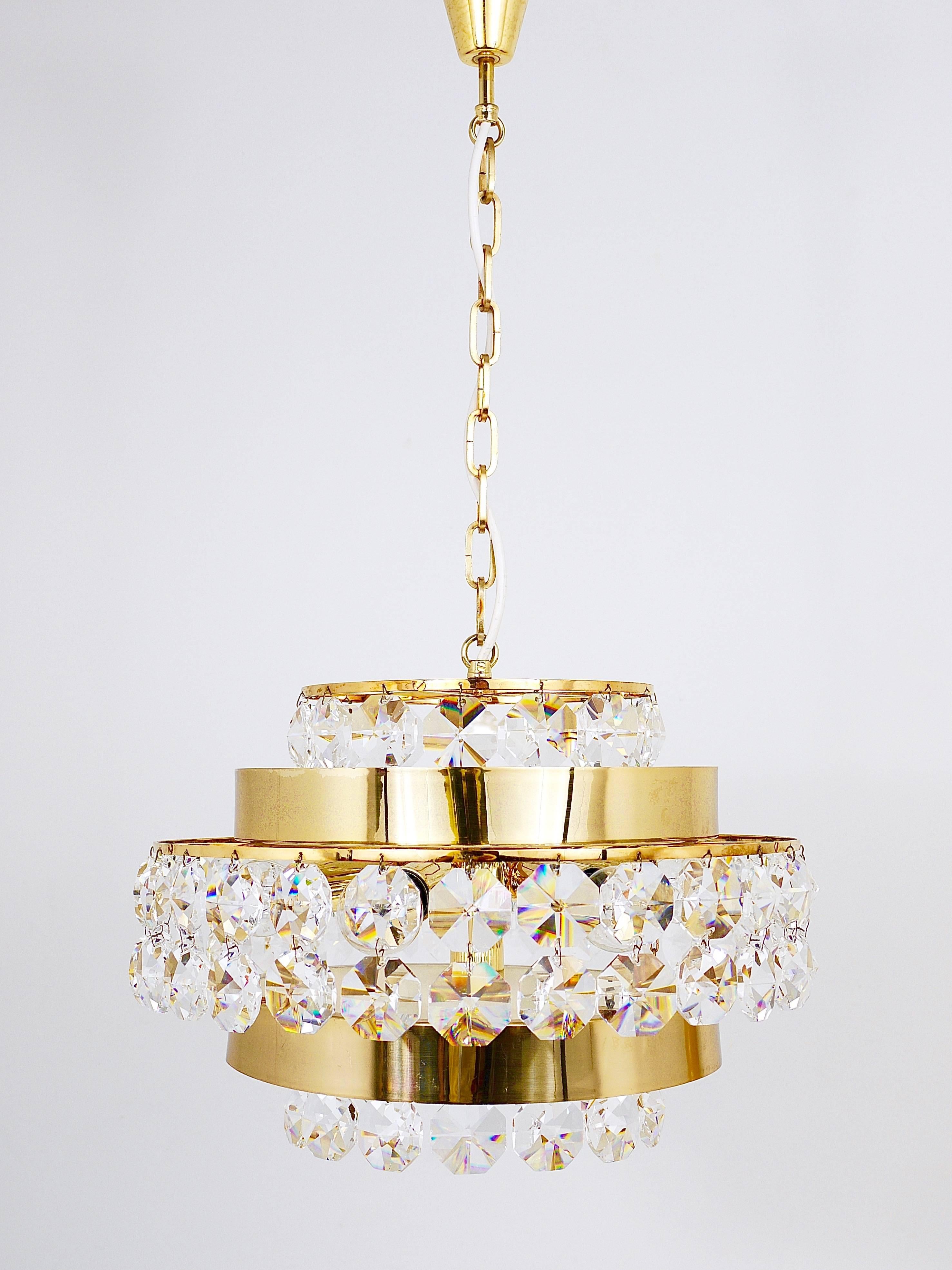 A beautiful gilt brass chandelier crafted in the 1970s by Bakalowits & Sohne of Austria. This exquisite piece features three tiers adorned with large, octagonal diamond-shaped faceted crystals and is illuminated by six light sources. In very good