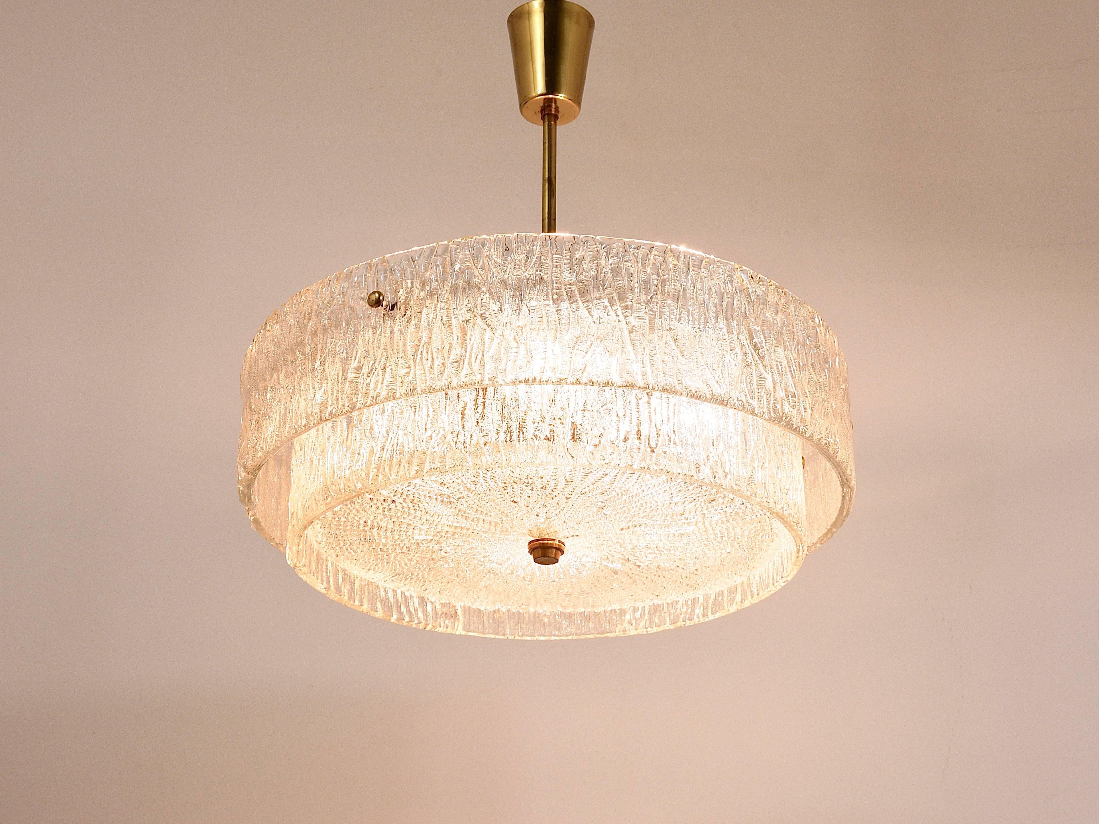 A beautiful modernist brass chandelier from the 1950s. Executed by Kalmar, Austria. Has two big glass rings made of textured ice glass. White painted base with brass rod and nice brass knobs. In very condition with marginal patina on the brass.