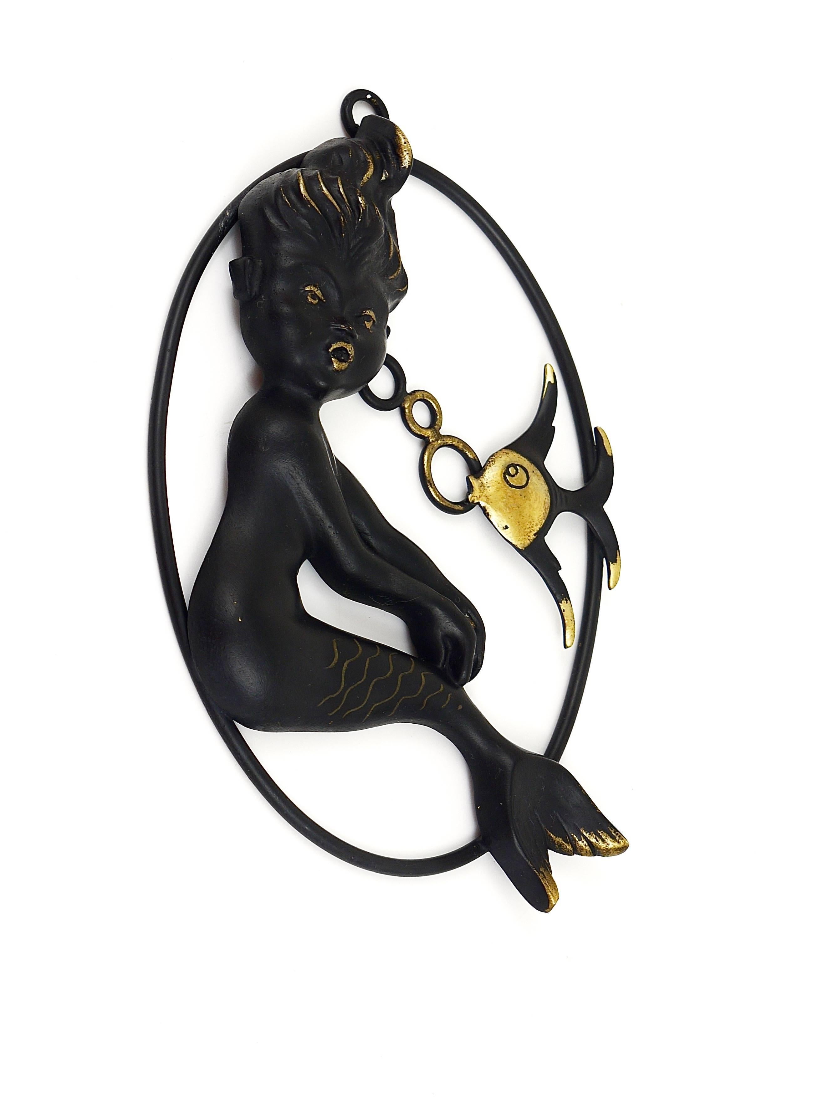 A lovely Mid-Century wall-mounted brass sculpture, displaying a mermaid and a fish on a frame, made of black-finished brass. Designed by Walter Bosse, manufactured in the 1950s by Hertha Baller, Austria. In excellent condition. A very decorative