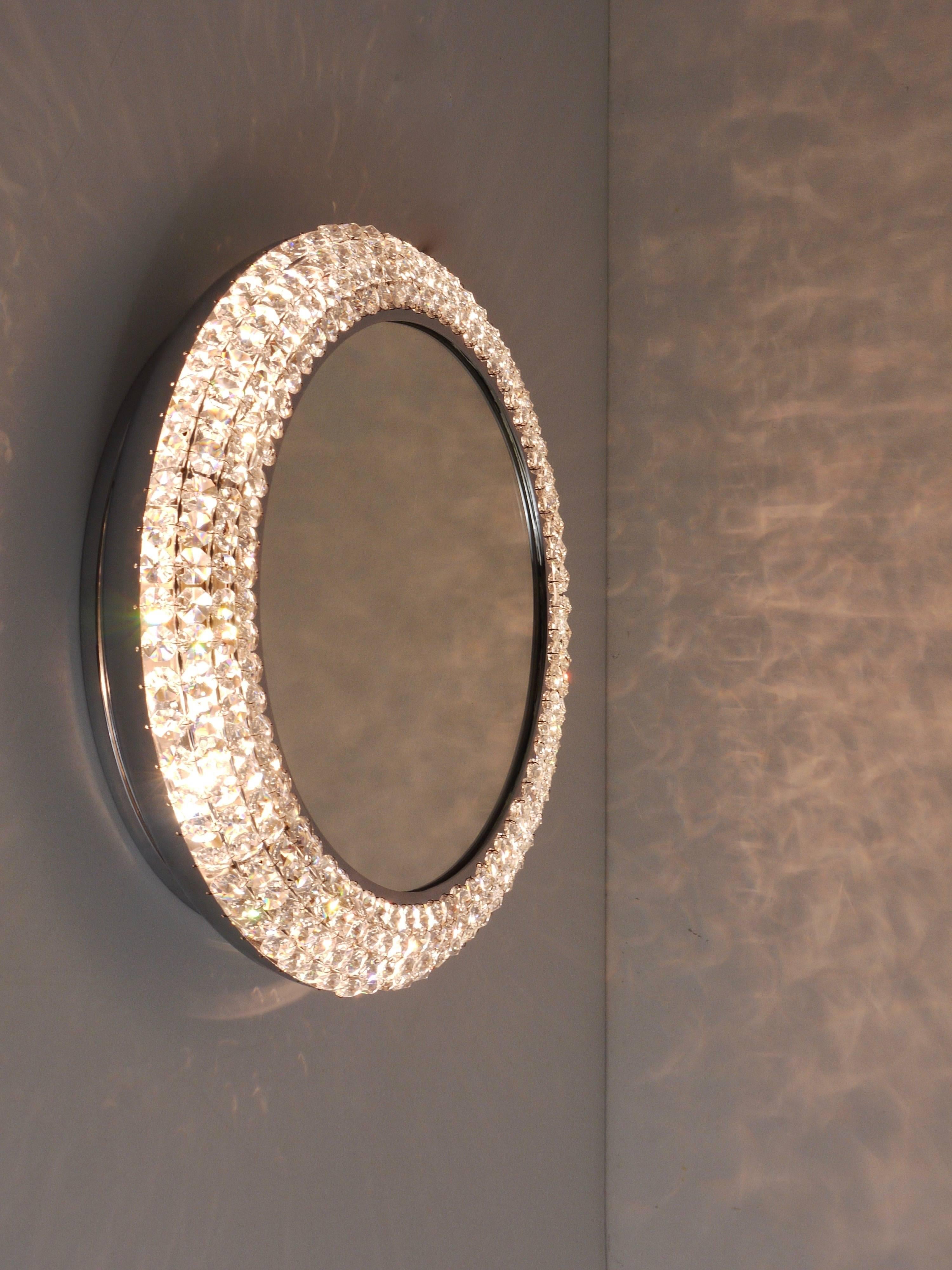 Exquisite round Mid-Century wall mirror, illuminated and encased in a chrome-plated frame covered with hundreds  of faceted crystals. Handcrafted in Austria during the 1960s, this handmade piece exemplifies excellent quality. It features four light