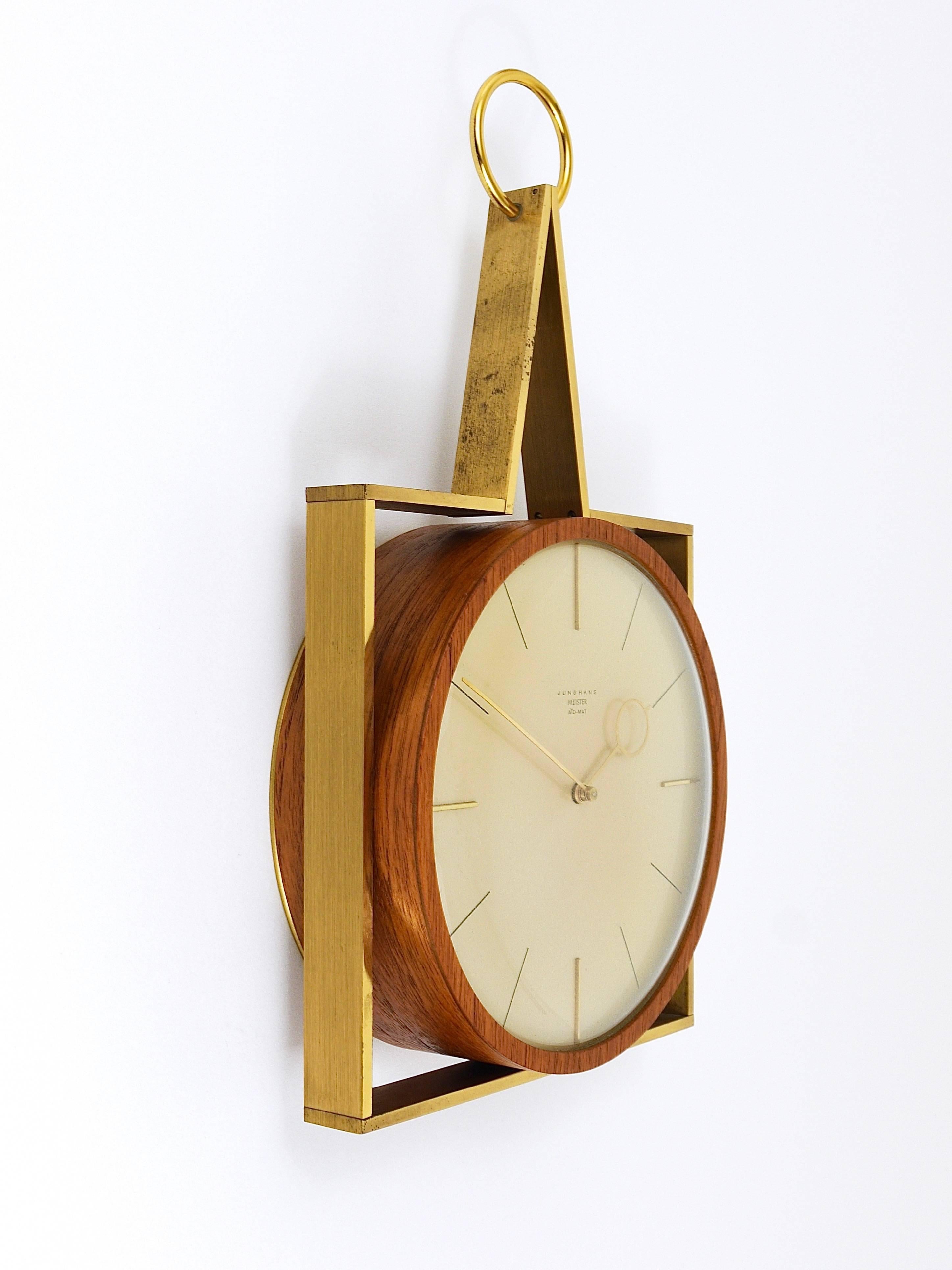An elegant and straight modernist wall clock with beautiful brass hands, a round teak wood housing and a square brass frame around. Executed in the 1950s by Junghans Germany. Powered by its original battery-operated movement. In very good condition