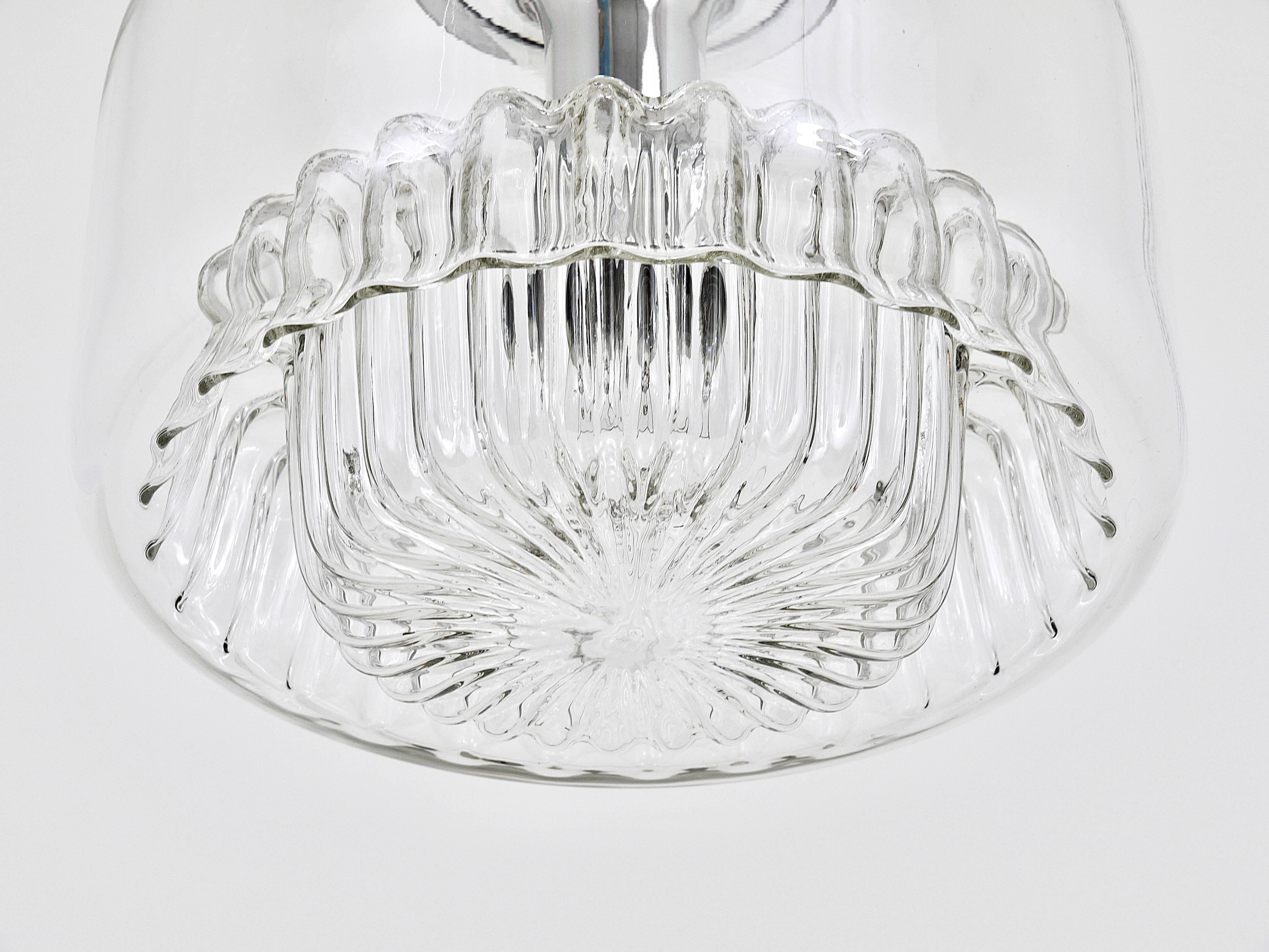 Up to two exquisite modernist pendant lights from the 1970s, each sold individually and priced per item. These stunning lights feature globe-shaped lampshades made of clear molded glass, complemented by chromed fittings. Crafted by Peill and Putzler