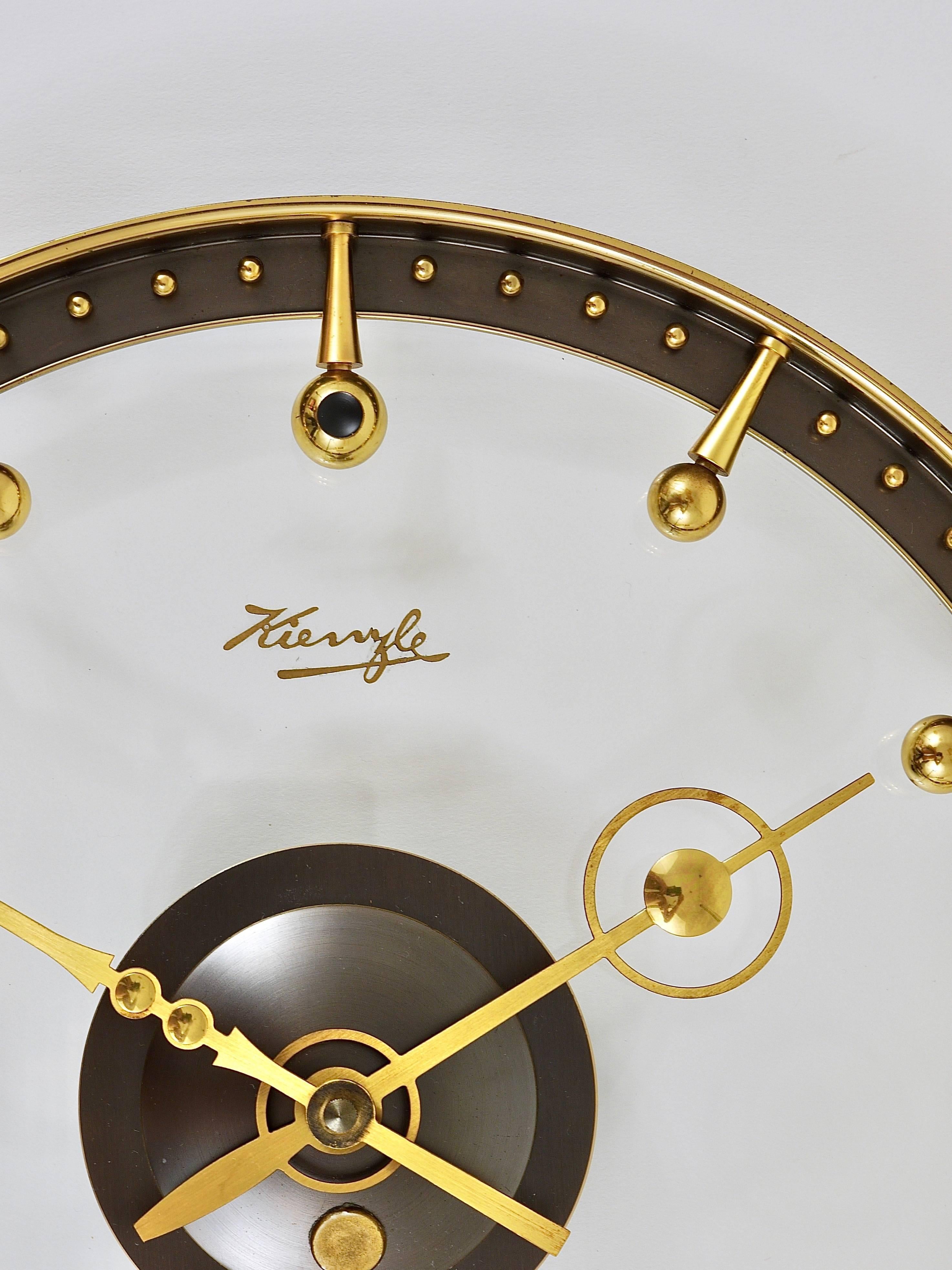 A beautiful and rare modernist wall clock from the 1950s, designed and executed by Kienzle Germany. A very unusual timepiece with a clocks face made of clear glass with stylish details like beautiful brass indices and hands. Powered by a standard