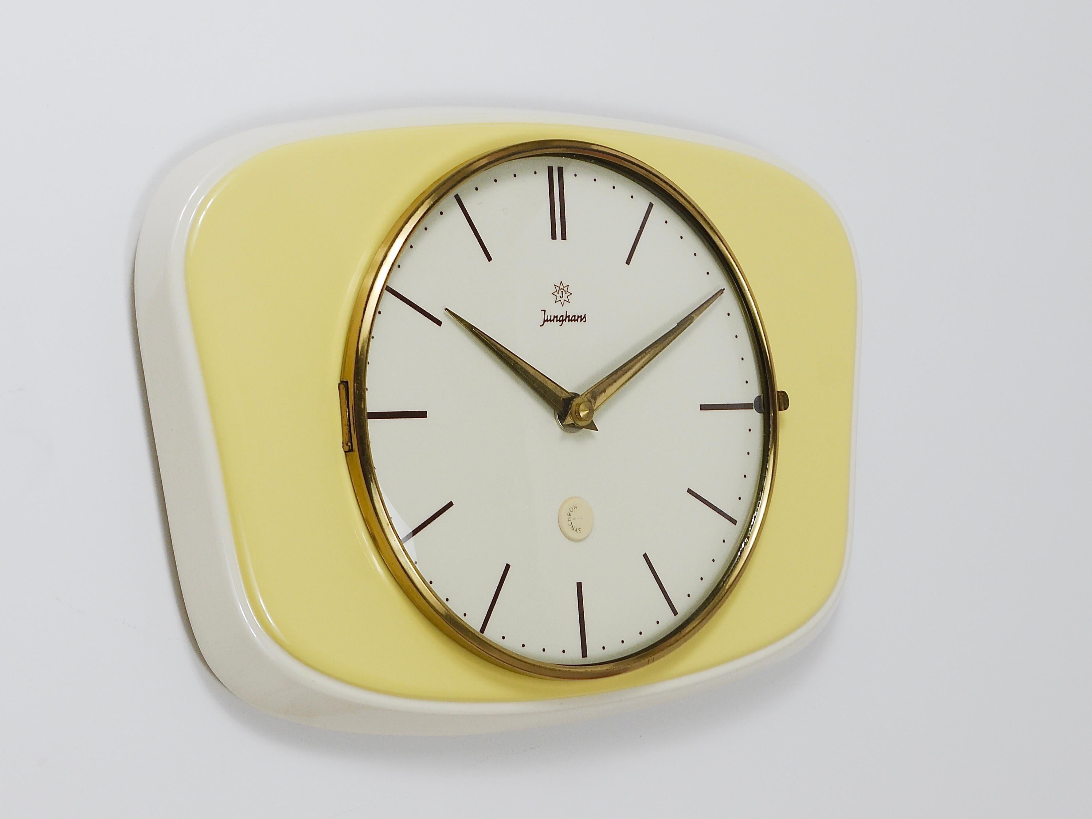 A lovely rectangular mid-century wall clock in landscape format, crafted by Junghans in Germany during the 1950s. Designed in the characteristic style of the era, it features elegant brass hands, a brass frame with domed glass, and a ceramic housing