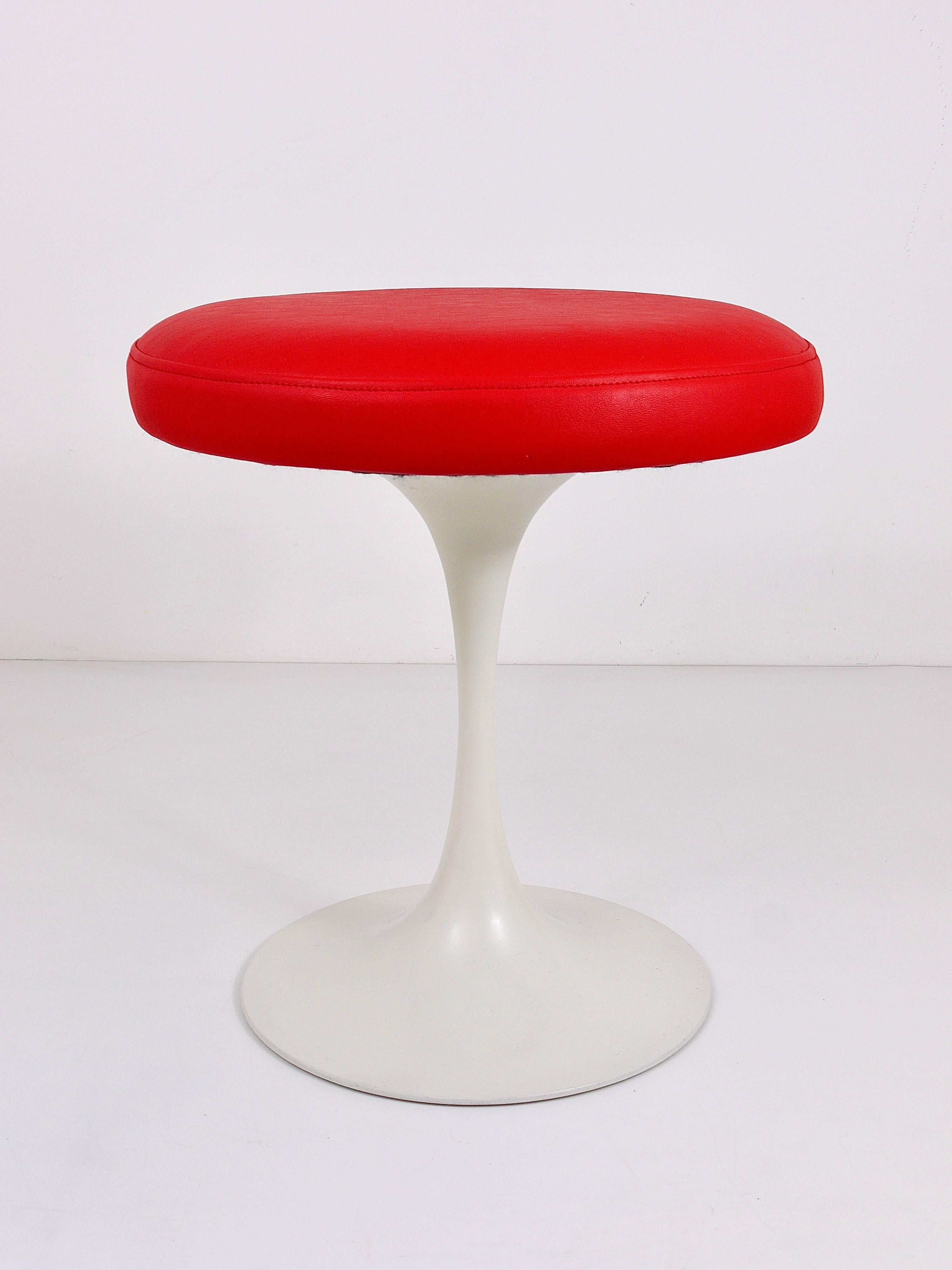 A beautiful space age stool from the 1960s, featuring a white tulip base and vibrant red faux leather upholstery. This piece, designed by Maurice Burke for Arkana in the United Kingdom, echoes the style of Eero Saarinen's designs for Knoll. The