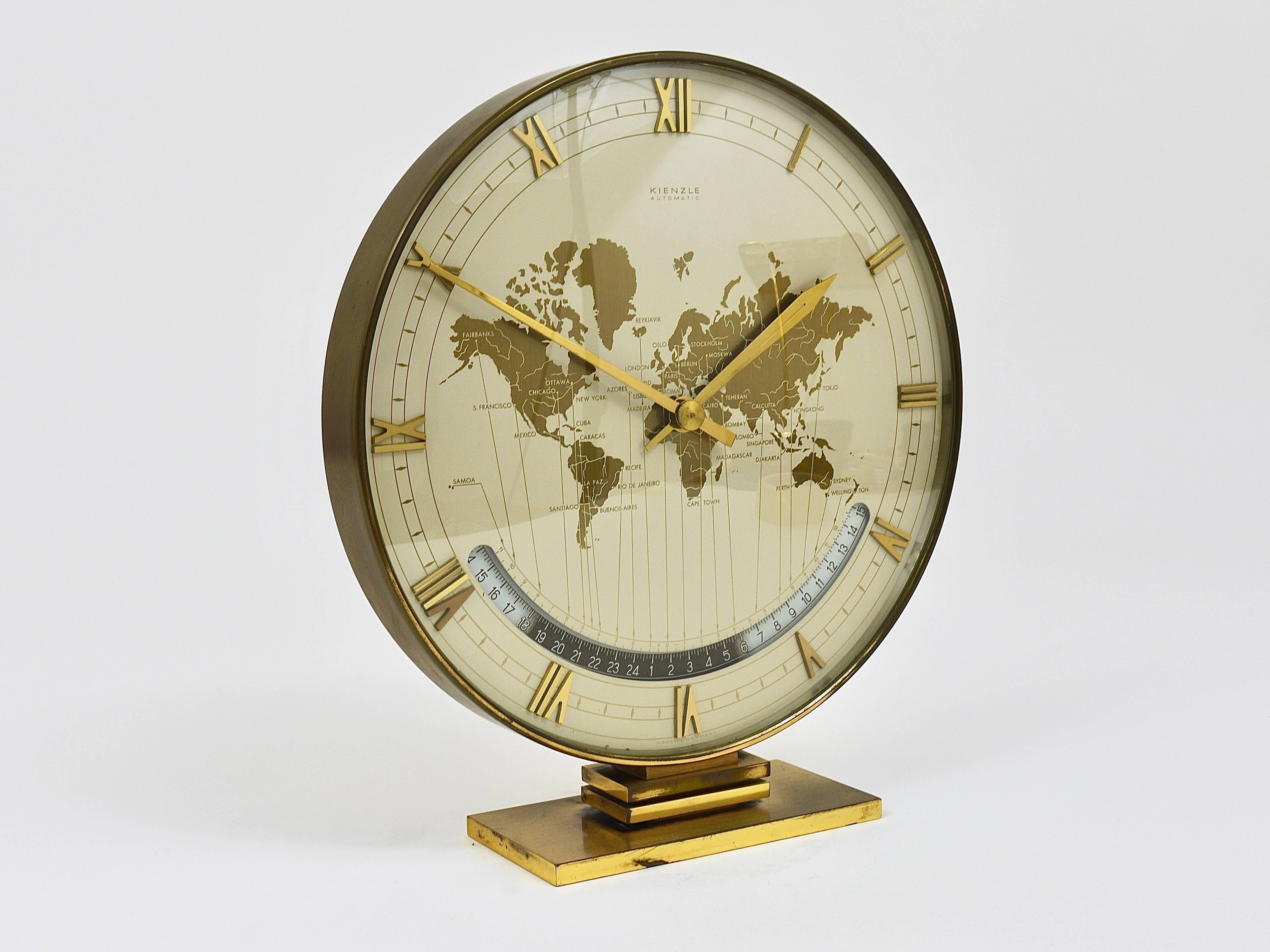 An impressive and large brass and glass modernist desk or table clock with a world map clocks face and world time zones and beautiful digits. Executed in the 1950s by Kienzle Germany. An elegant and solid piece in good condition with charming patina
