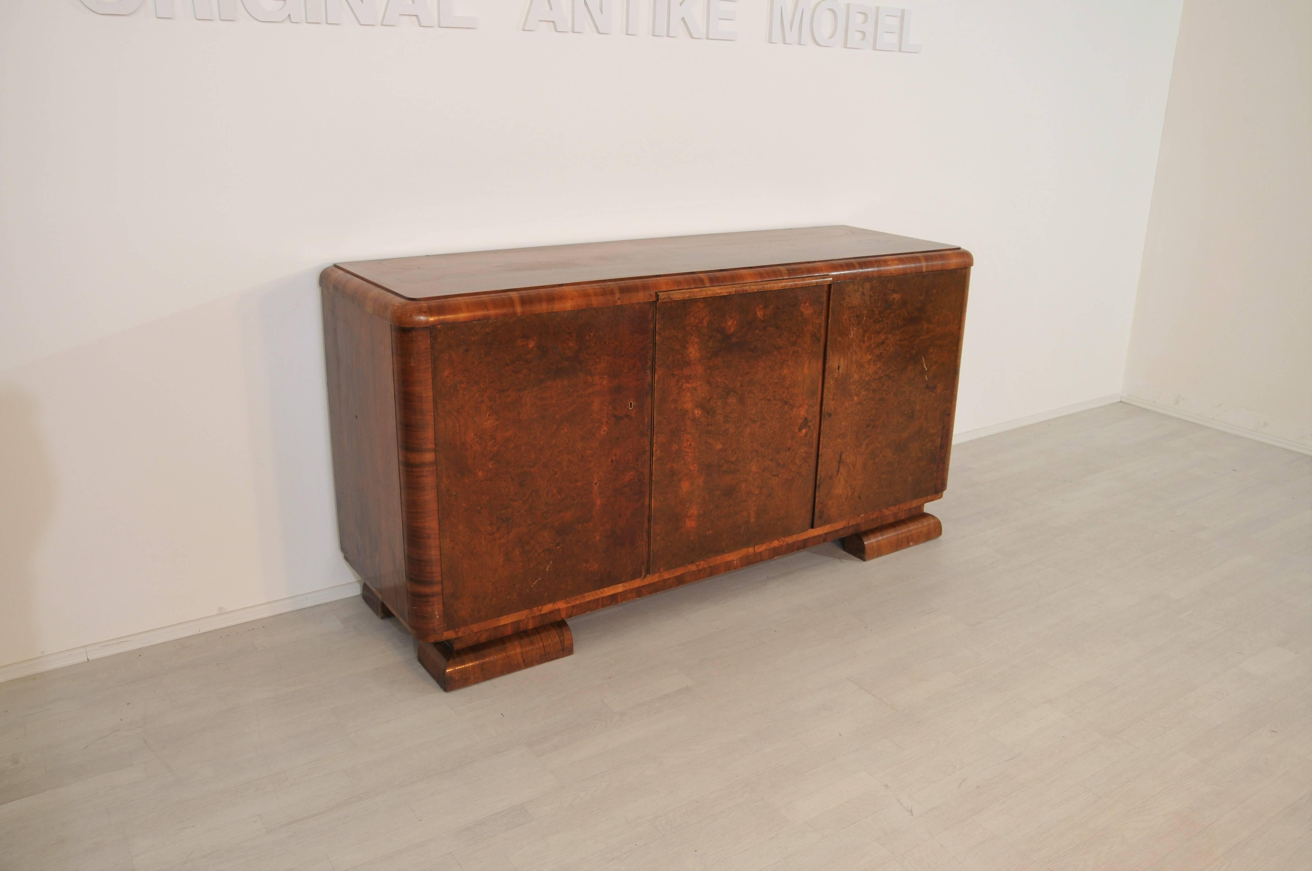 Original piece of furniture from the Art Deco epoch with a big surface area. The sideboard consists of wonderful burl wood with a unique texture. Behind the left door you will find two drawers, behind the middle and right doors you can adjust the