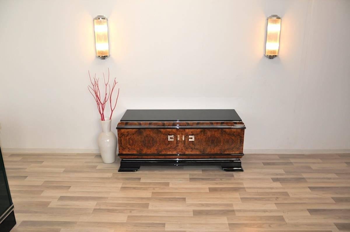 Art Deco lowboard or commode with doors made of wonderful walnut wood. This petite masterpiece offers a great veneer and details made of piano lacquer. Perfect small storage space with a luxurious design and a lacobel glass plate on top for everyday