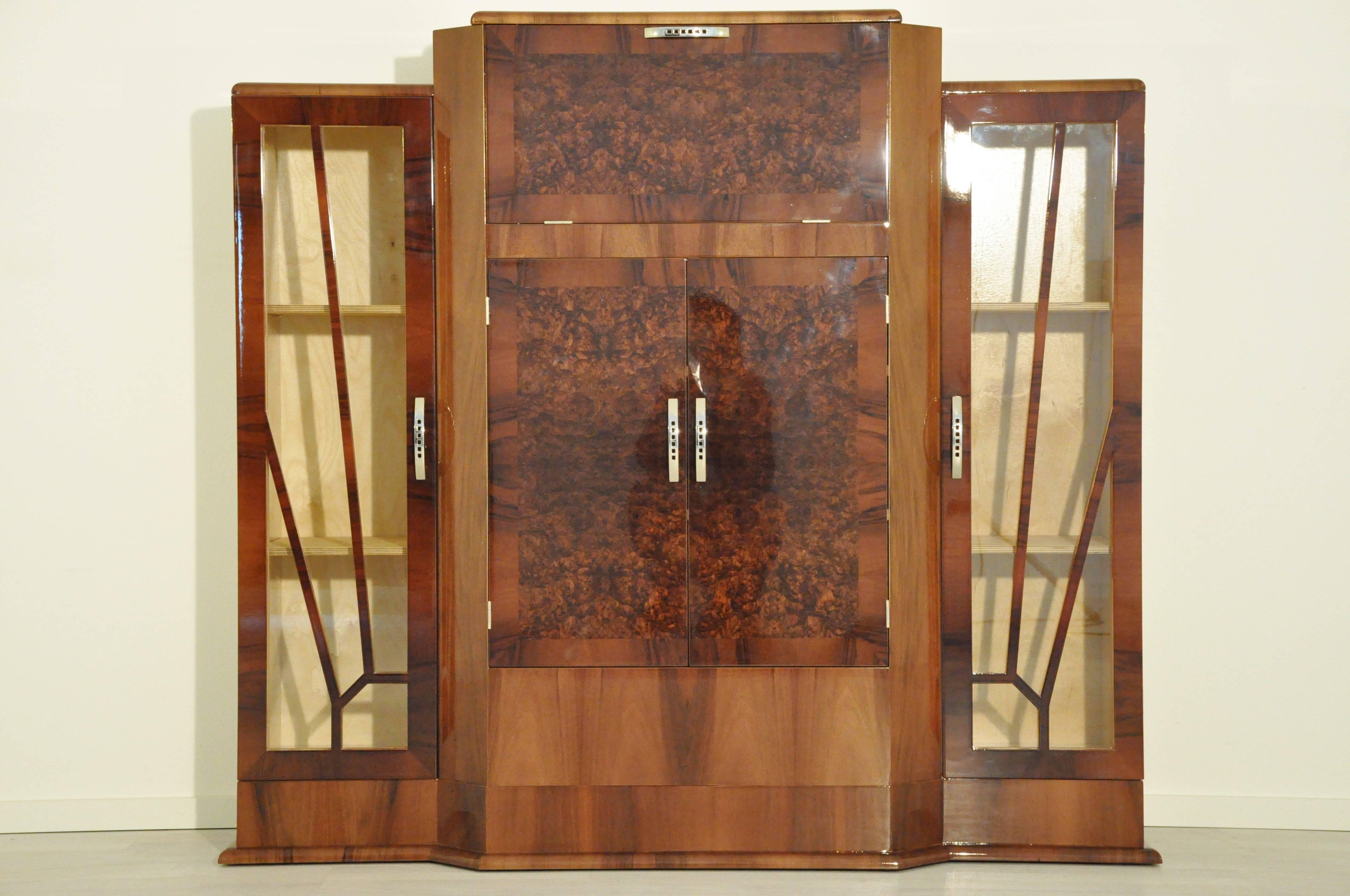 Great Art Deco bar cabinet made of gorgeous walnut wood with different grains. It offers a typical Art Deco design, a serving area with mirrored panels, and two big showcase compartments on the sides. This special piece of furniture was build by