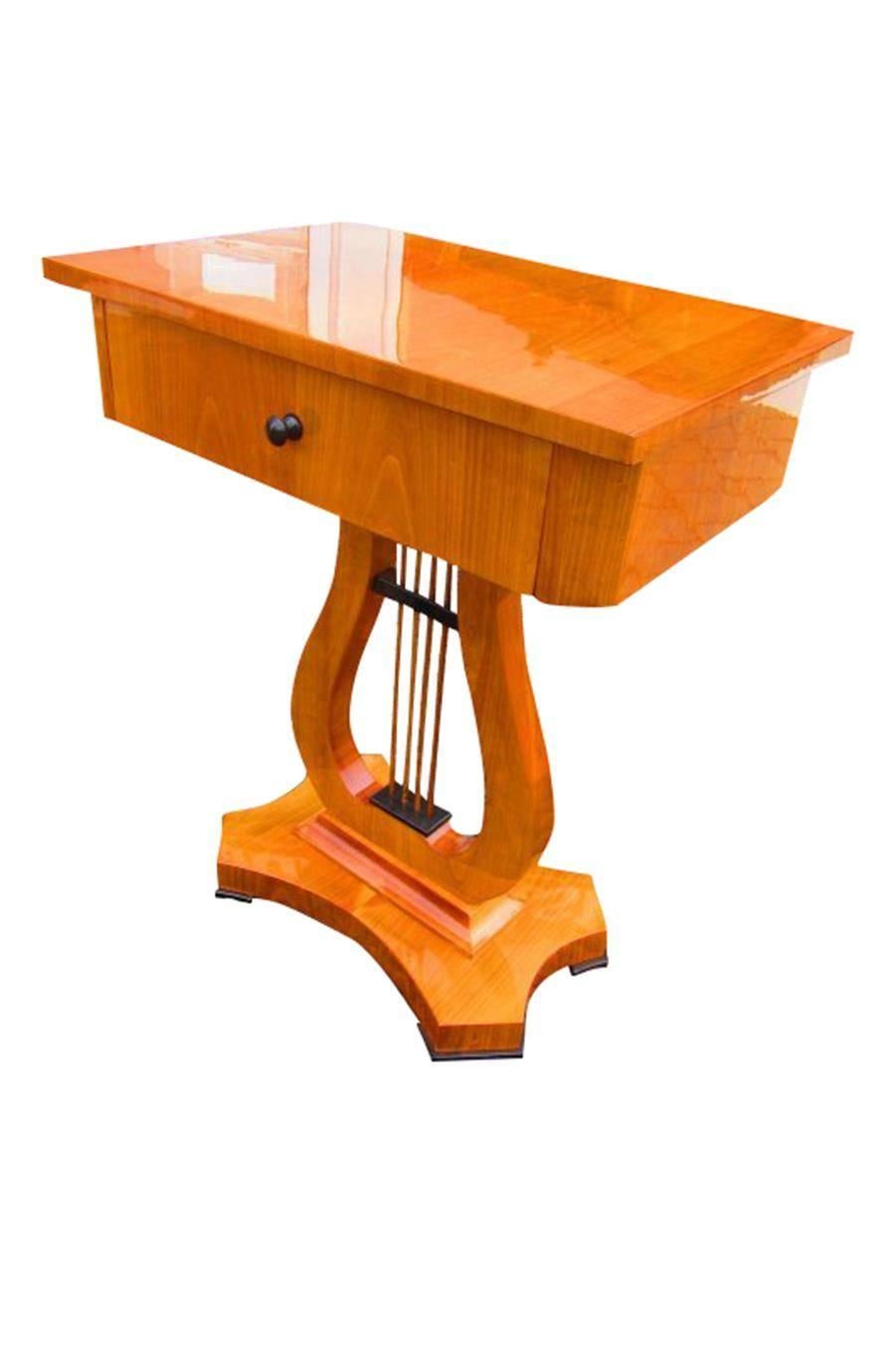 This artful sewing table with Biedermeier design consists of massive cherry tree wood. The surface is high gloss polished and in a excellent condition.

- elegant design with fine details and a front drawer
- perfect reproduction after original
