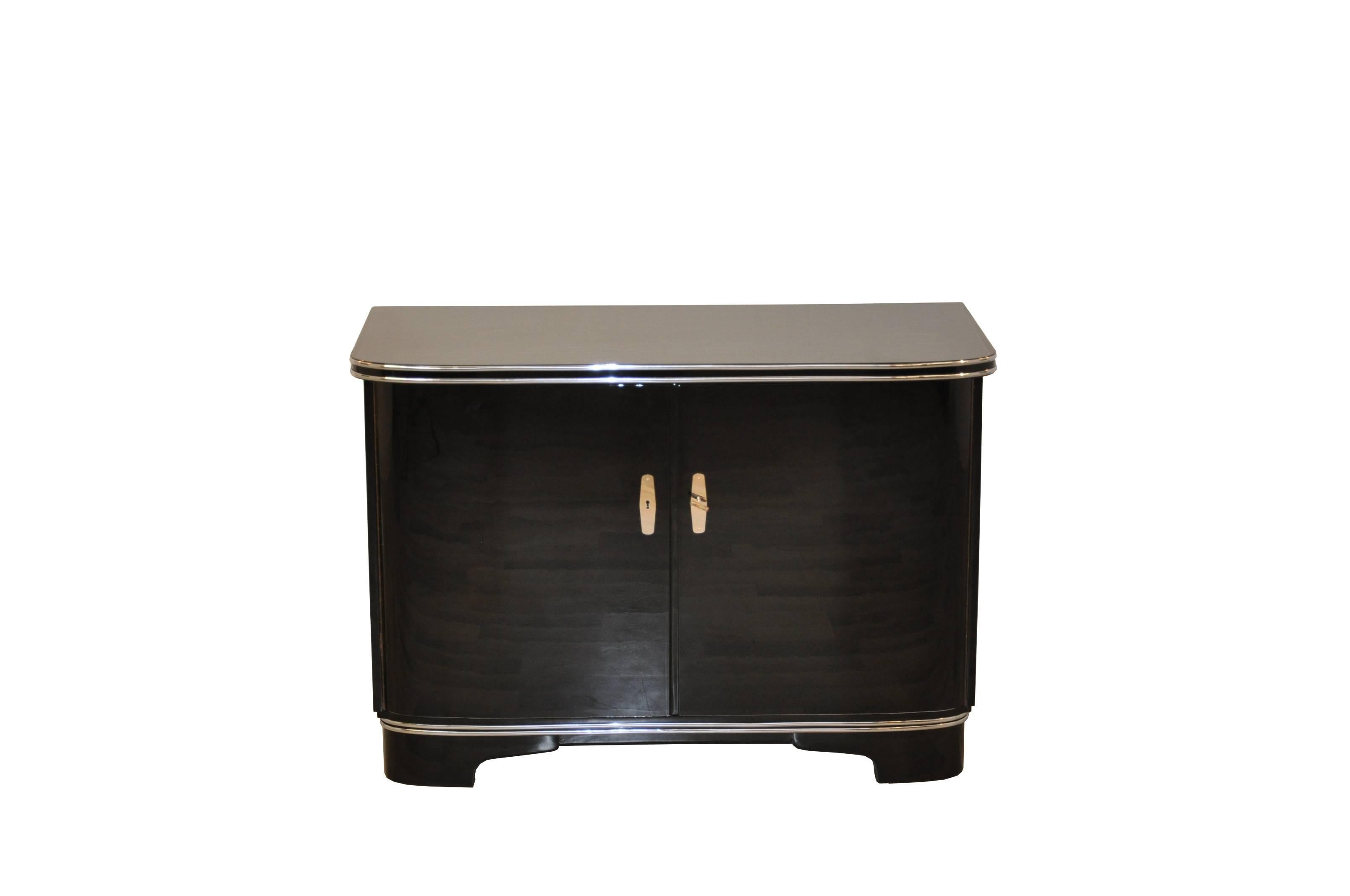 A small Art Deco commodes lacquered with black piano lacquer. This chest of drawers has been restored to the finest detail in our manufactory and now shines with a new look. Fine chrome lines surround the plate and the foot and is finished with a