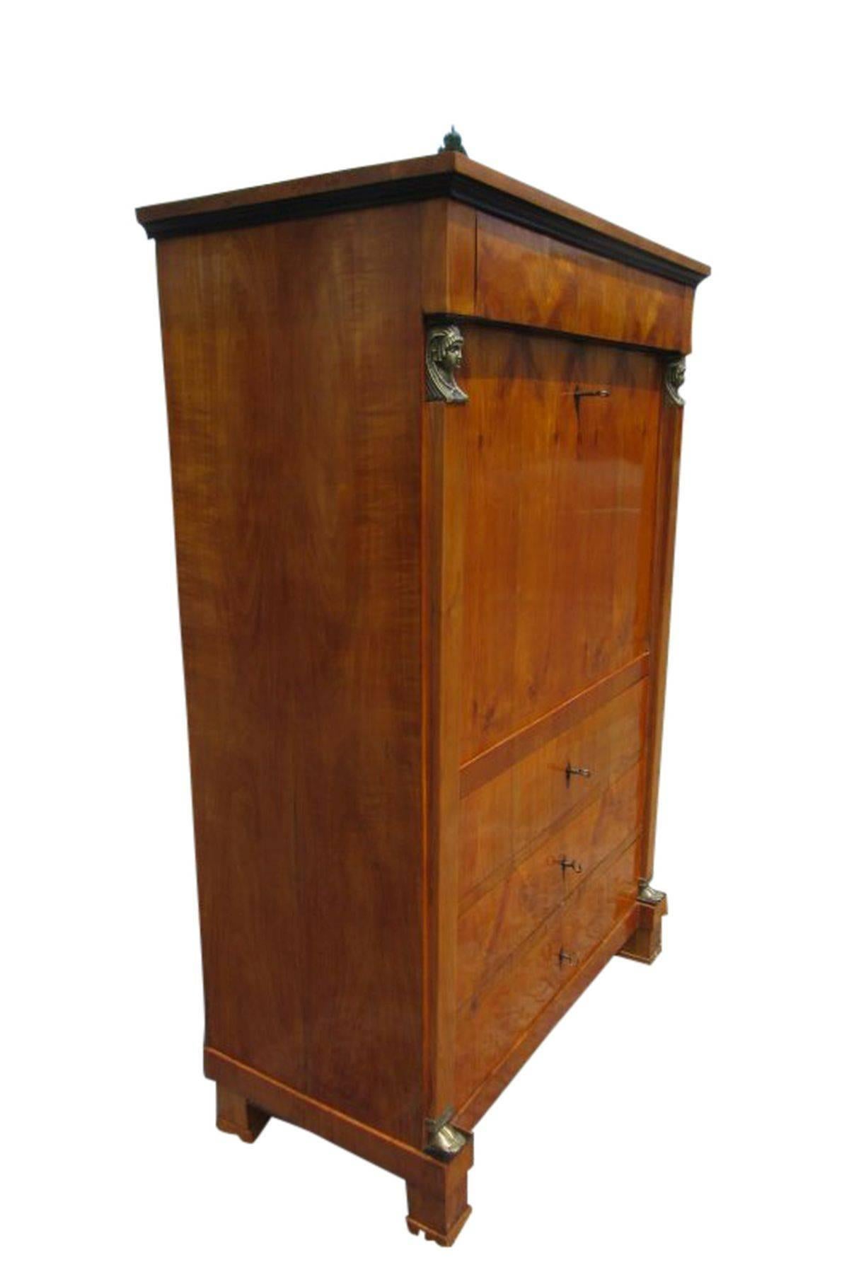Biedermeier secretary made of cherrywood. It has a big interior with 11 small drawers and four big drawers. The intelligent design has a lot of use and looks wonderful. The woman's heads on both side create are made of brass and create a unique