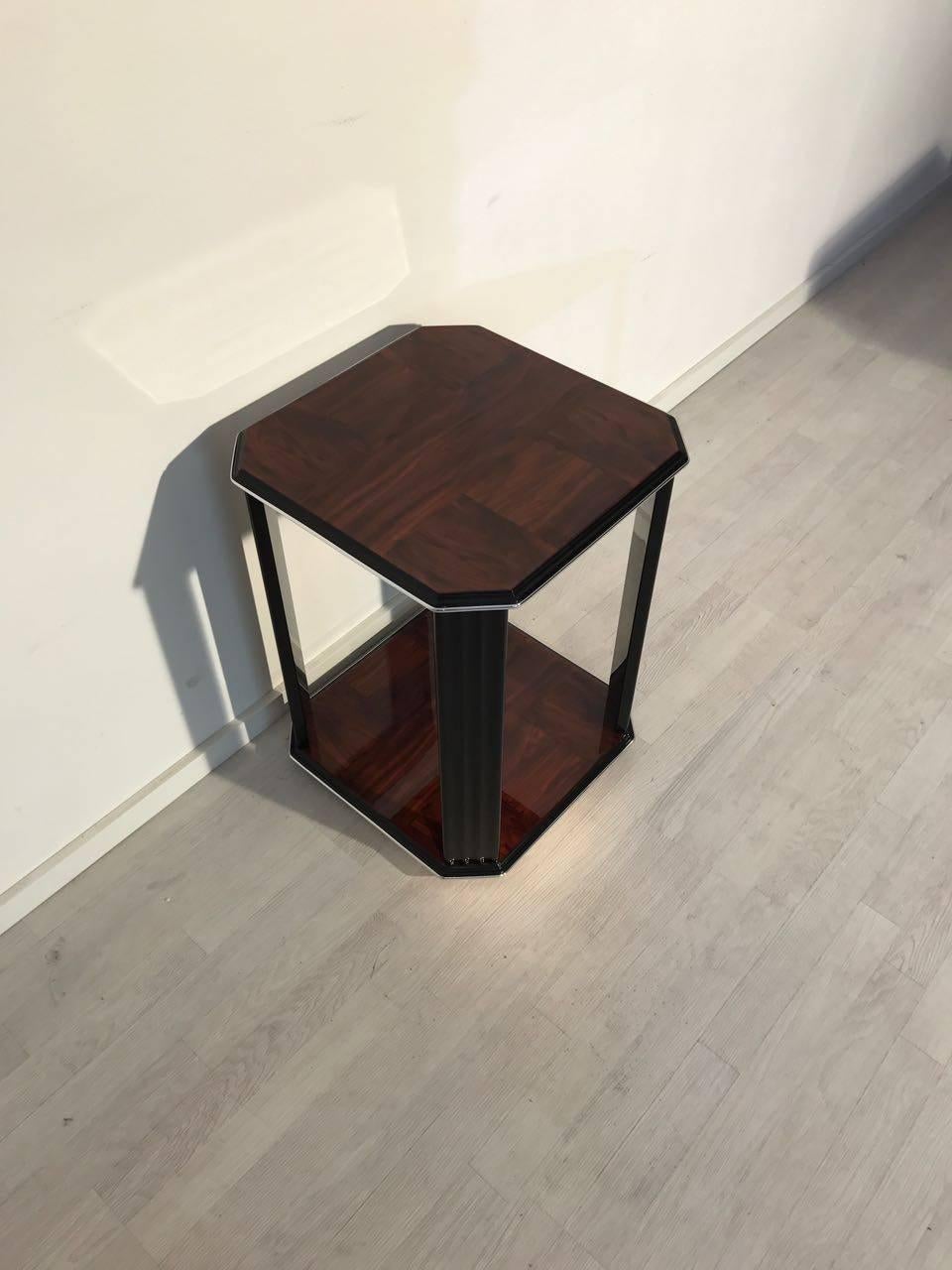 An Art Deco coffee table in mahogany. The upper plate, as well as the lower, is veneered with miraculous mahogany and has a brilliant grain. The brown veneer combined with the excellent black piano lacquer make a great coloring game. Circular chrome