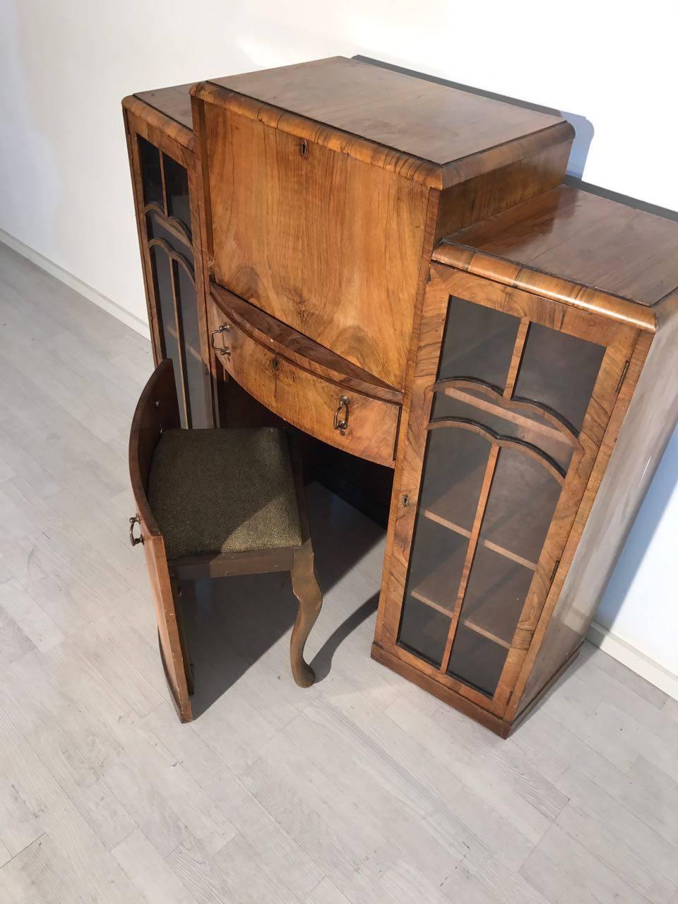 An Art Deco secretary in walnut wood. It offers a typical Art Deco design with glass doors accentuated by wood adornments, as well as integrated seating options. The brown wood has a wonderful grain and a great coloring game. The secretary is