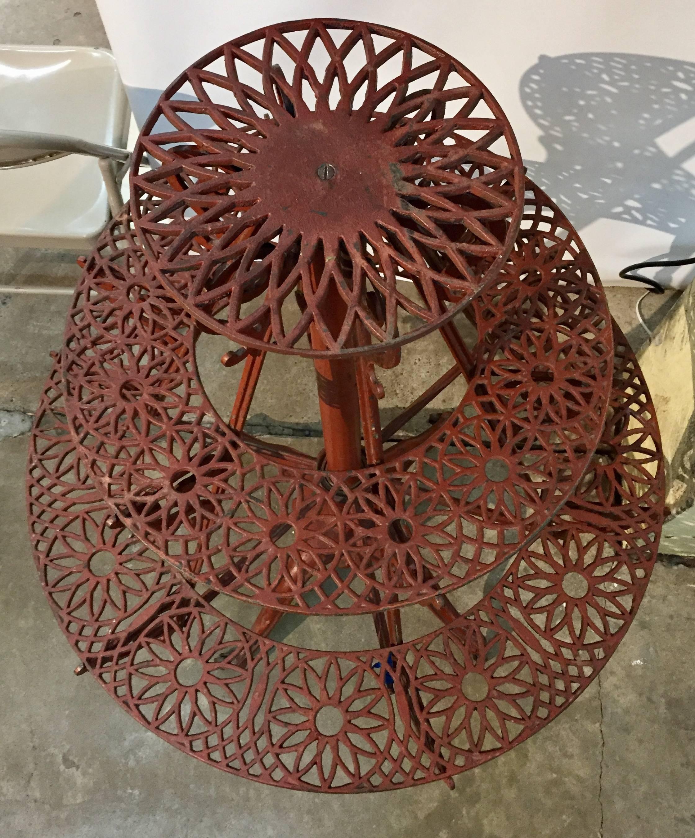 A highly refined and developed stand in the round, having three rotating graduated cast iron shelves, on a columnar shaft, standing on a cast iron quadripartite base; in an appealing and attractive red paint surface.