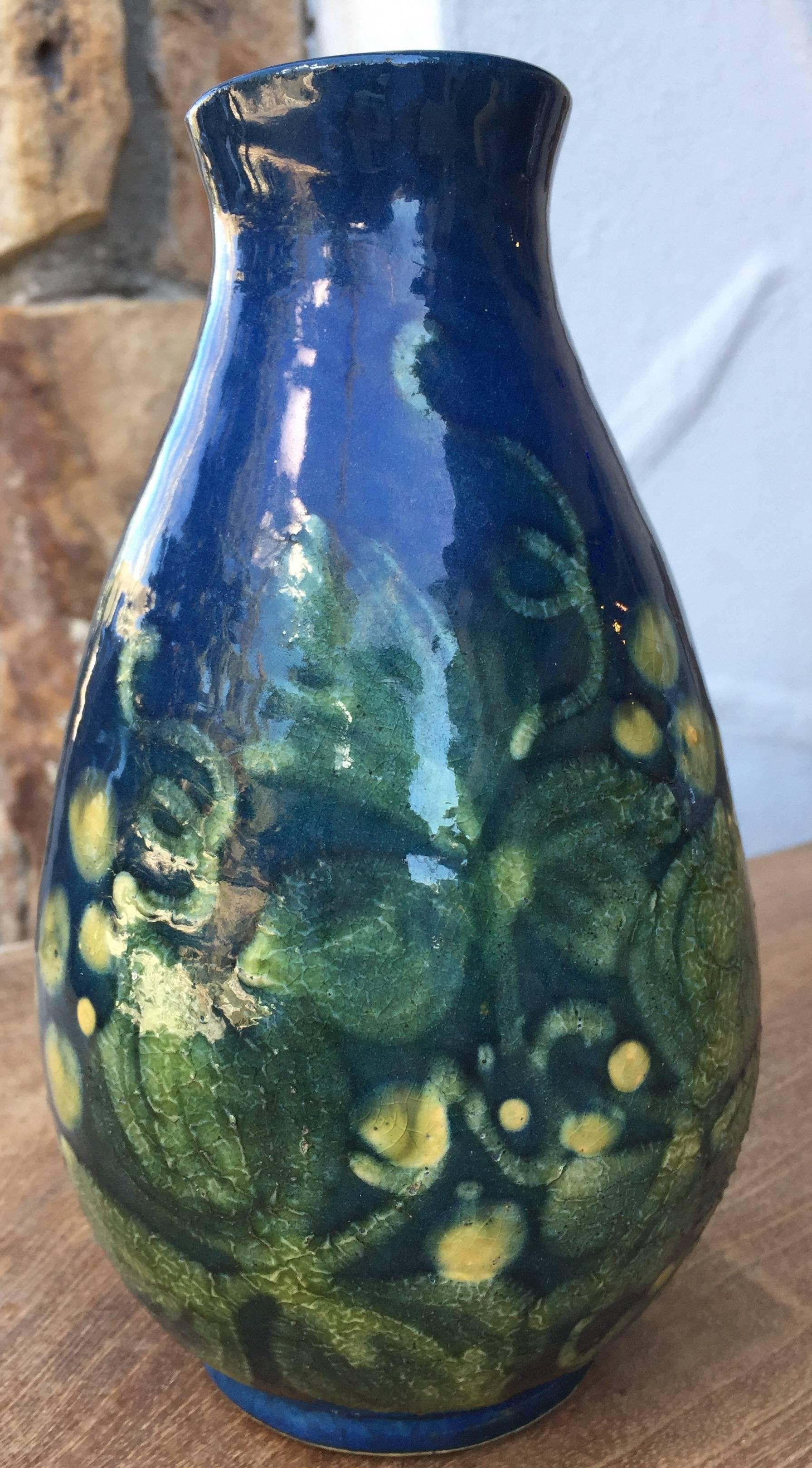A French ceramic vase. Bulbous form base tapers upwards to a round opening. Body of vase is decorated with green and faint ivory floral motifs over a dark blue ground. Underside is impressed 