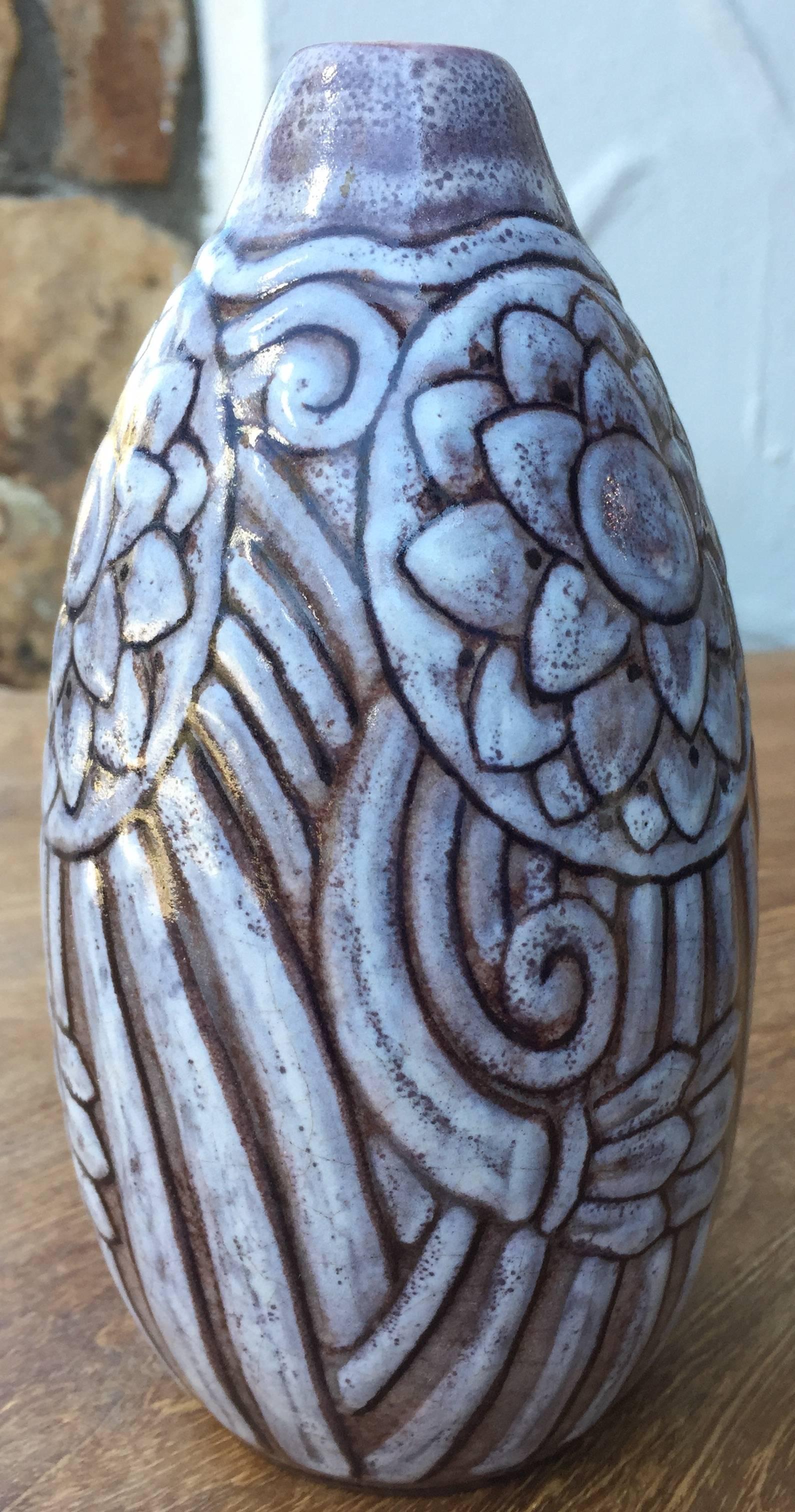 A French Art Deco glazed stoneware vase. Tapering upwards to a small opening. Mauve and grey glaze over high relief decoration of floral circles and curved lines throughout. Underside is signed 