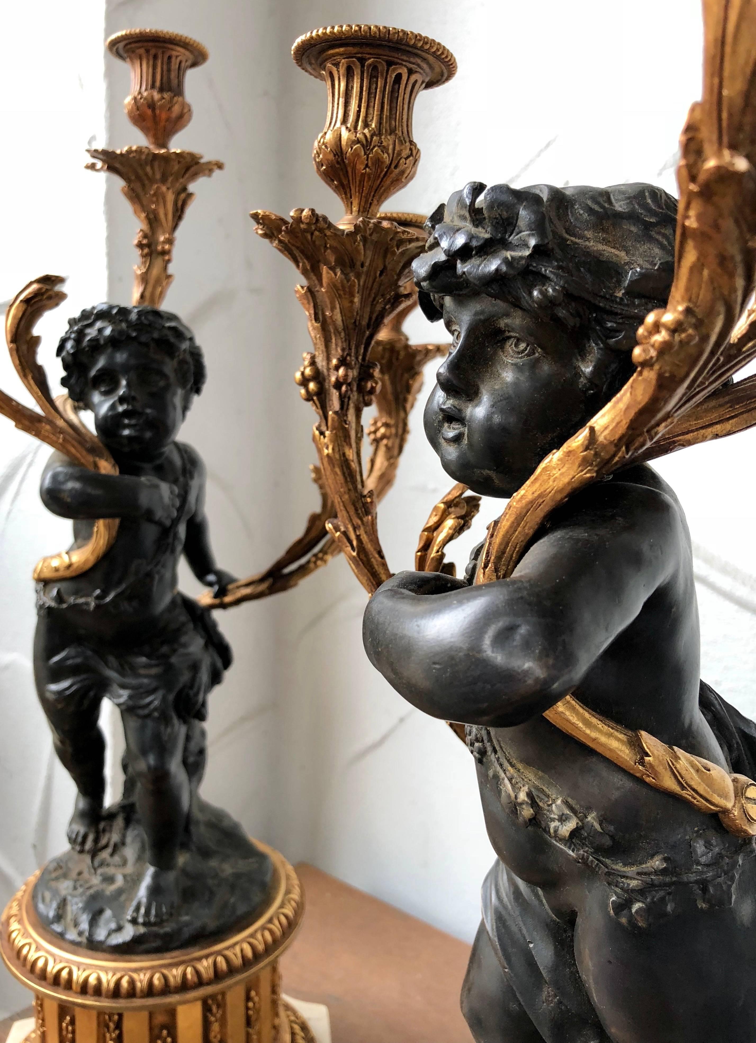 Pair of marble and bronze three-light candelabra. Bronze fluted plinth on a white marble base, bronze standing figure of a cherub holds three gilt bronze filigree branch candle holders in his arms; base and candle arms have a gilt finish, figure has