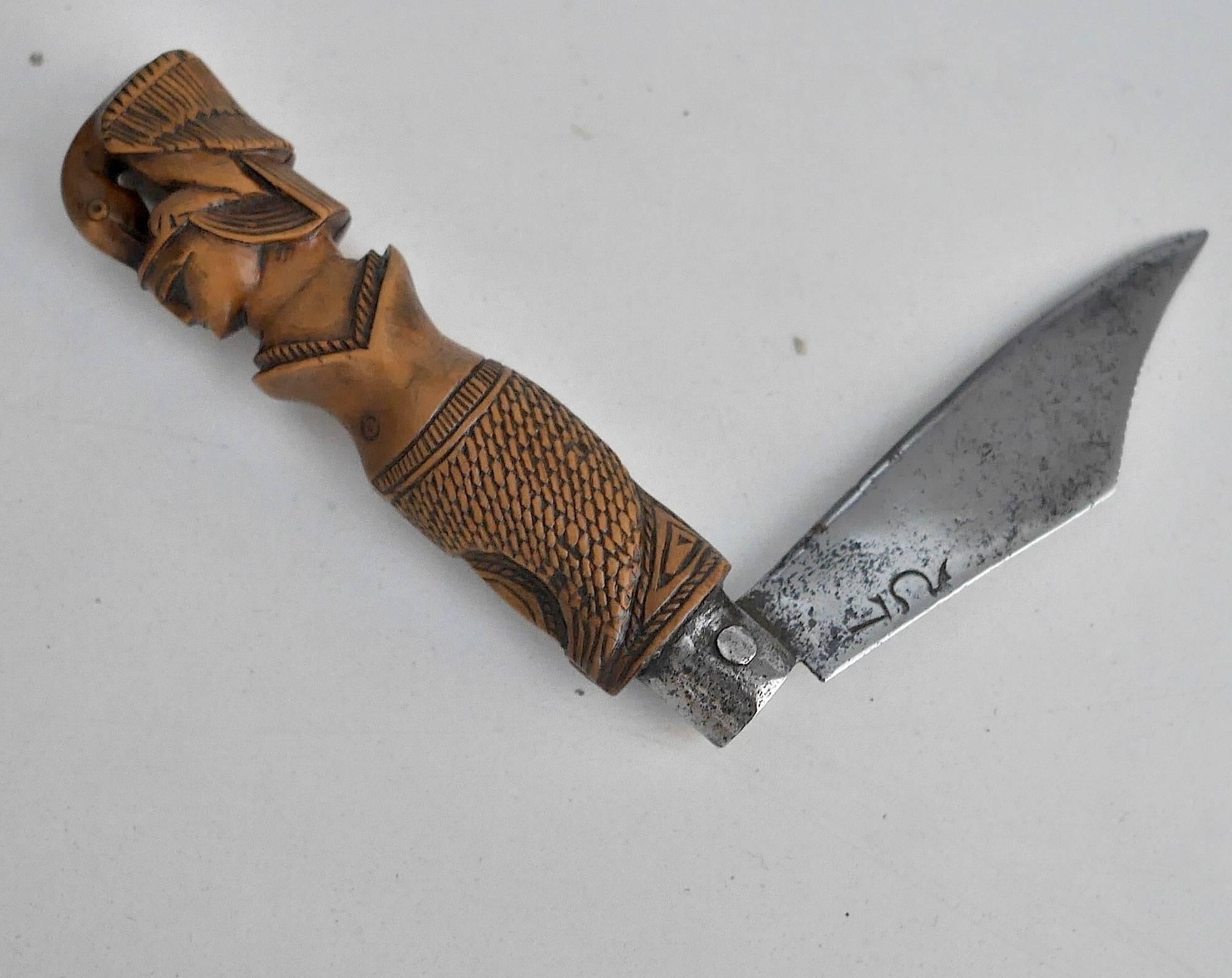 Maple tree sculpted Greek pocket knife with a carved handle featuring a fish with its mouth widely opened, a man and a bird. The blade is engraved with Greek letters, probably the initials of its owner.
 