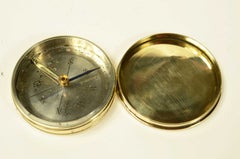 Small travel compass made of turned brass with a pink cover marked with the eight points of the compass