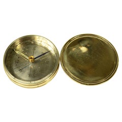 Small travel compass made of turned brass with a pink cover marked with the eight points of the compass
