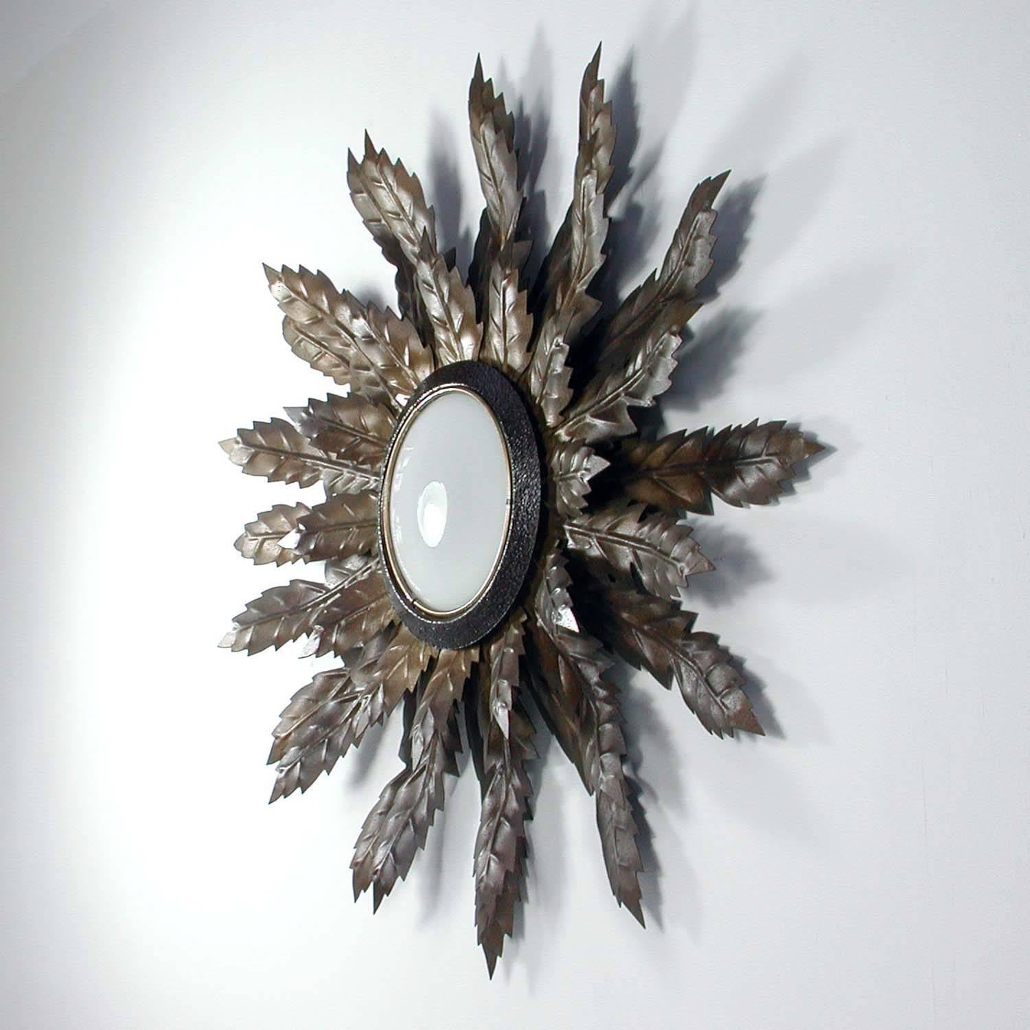 This Mid-Century sunburst sconce was produced in Spain in the 1950s. It is made of bronzed metal and has got a round opal glass lampshade.