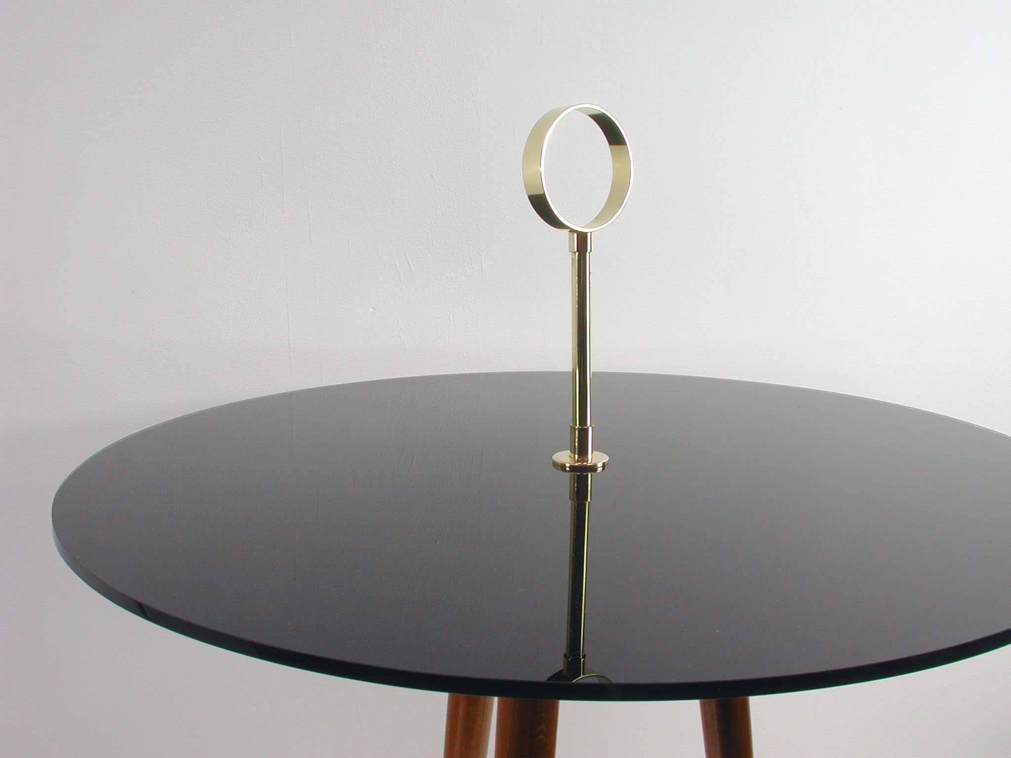 This tripod side table was made in Italy in the 1950s. It has got three teak legs with ball feet, a black glass tabletop and decorative brass details.
  