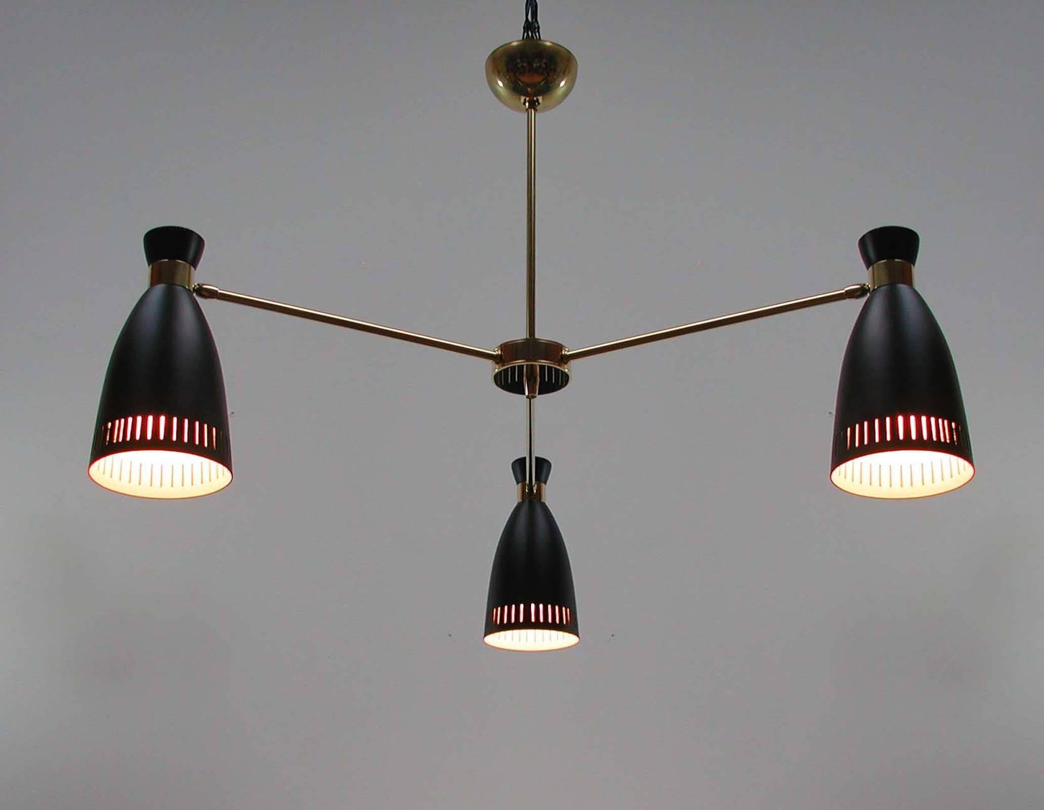 This three-tier chandelier was manufactured in Italy in the 1950s. It has got three adjustable cone shaped black lacquered metal lampshades and brass Sputnik lamp arms.

The chandelier is in excellent condition with minor signs of use and age and