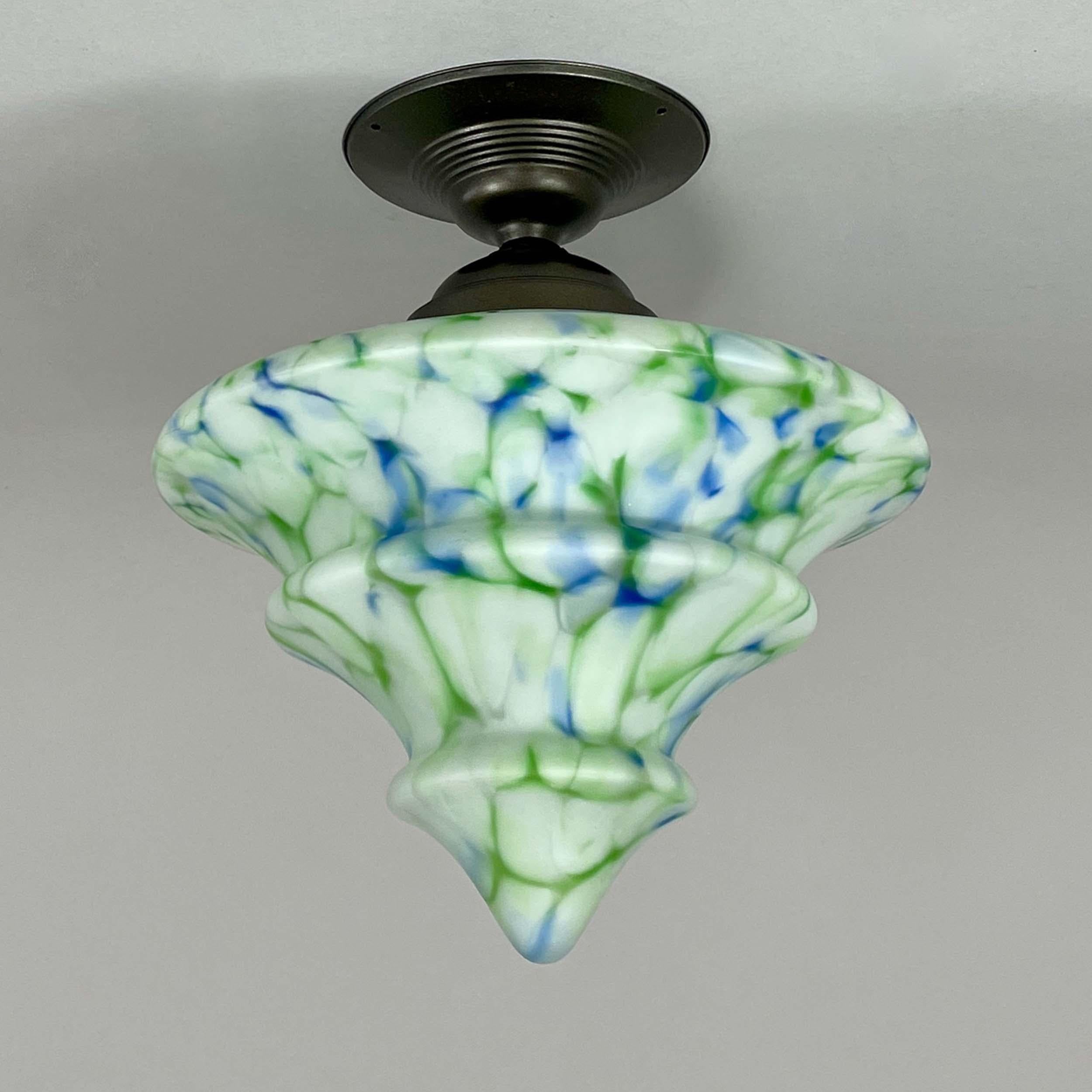 This Art Deco flush mount was designed any manufactured in Germany in the 1930s.

The light features a flared silhouette and tiered, geometric contouring. The hand-blown glass shade displays a marbled pattern in white with flowing streaks of emerald