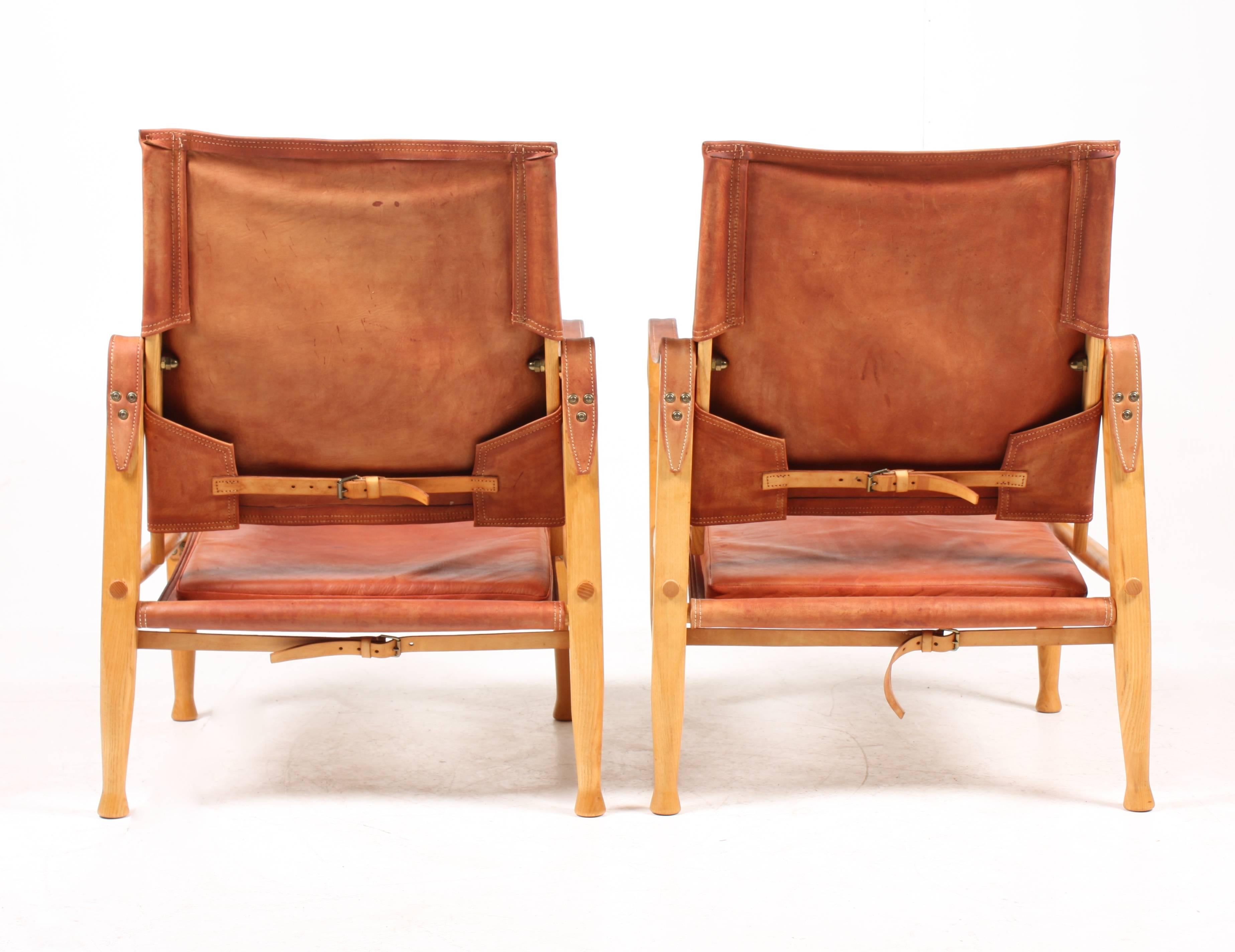 Pair of safari chairs in elm and well patinated reddish leather designed by Maa. Kaare Klint for Rud Rasmussen cabinetmakers in 1933. This pair is from the 1960s. Made in Denmark. Great original condition.