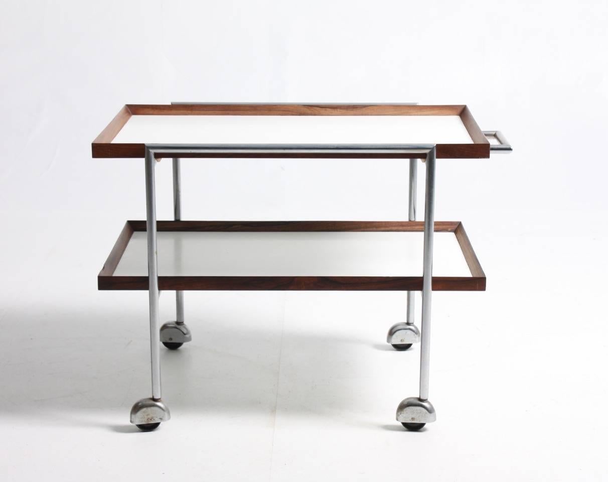 Trolley with a base of chromed metal and two serving trays in rosewood and white formica. Designed by Maa. Poul Nørreklit for E. Pedersen cabinetmakers. The trolley is made in Denmark in the 1960s. Great original condition.