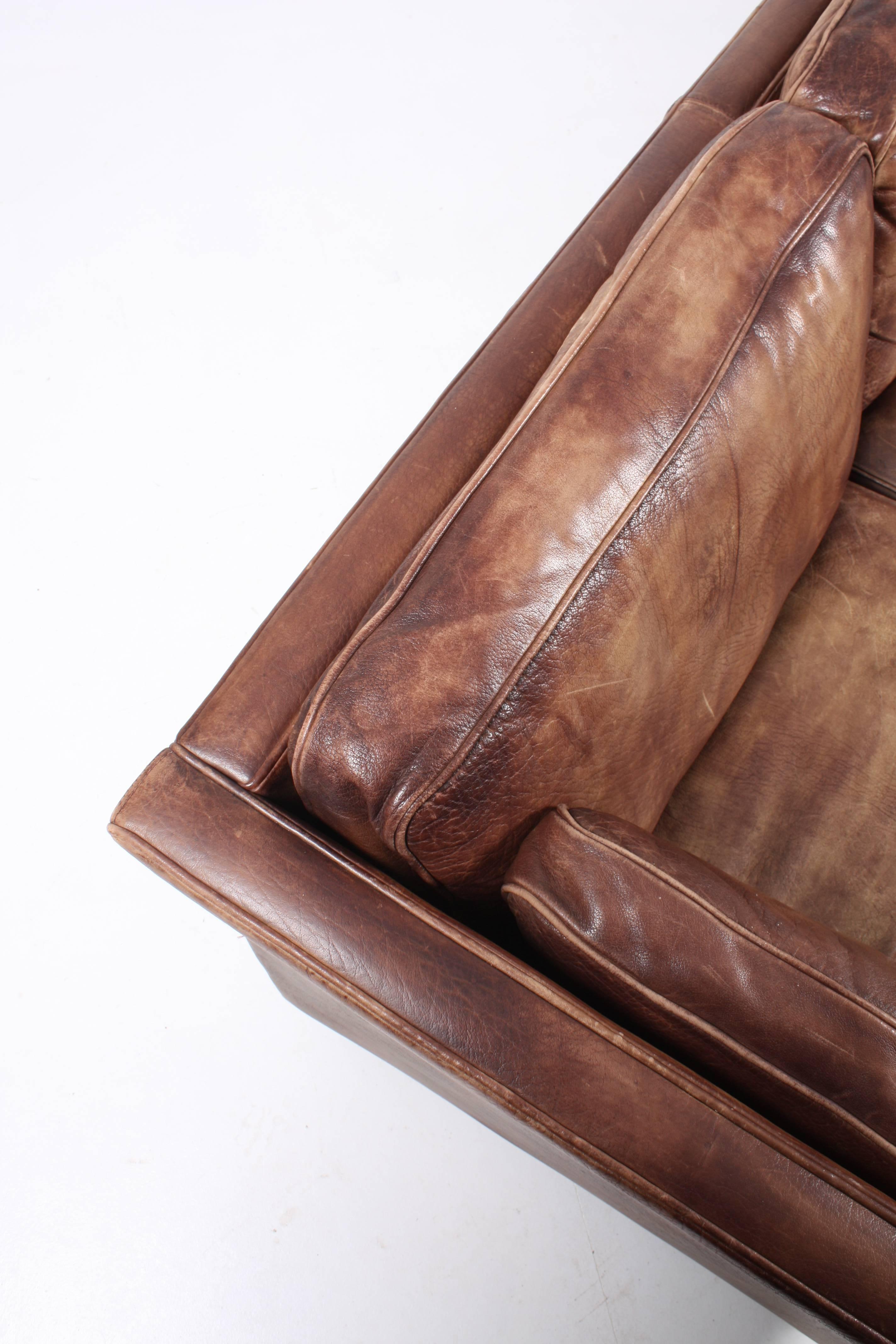 Great looking and very comfortable three-seat sofa in patinated leather standing on legs of solid mahogany. Designed and made in Denmark in the 1960s. Has been cleaned, waxed and is from a non-smoker home.