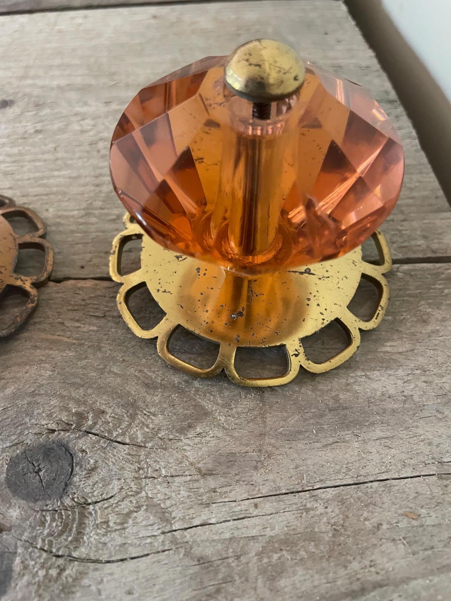 Se trata de tiradores y pomos Art Déco de cristal y latón dorado. El cristal es de un color difícil de distinguir, coral o rosa.
Las medidas de diámetro y altura corresponden a los tres pomos de mueble más grandes.